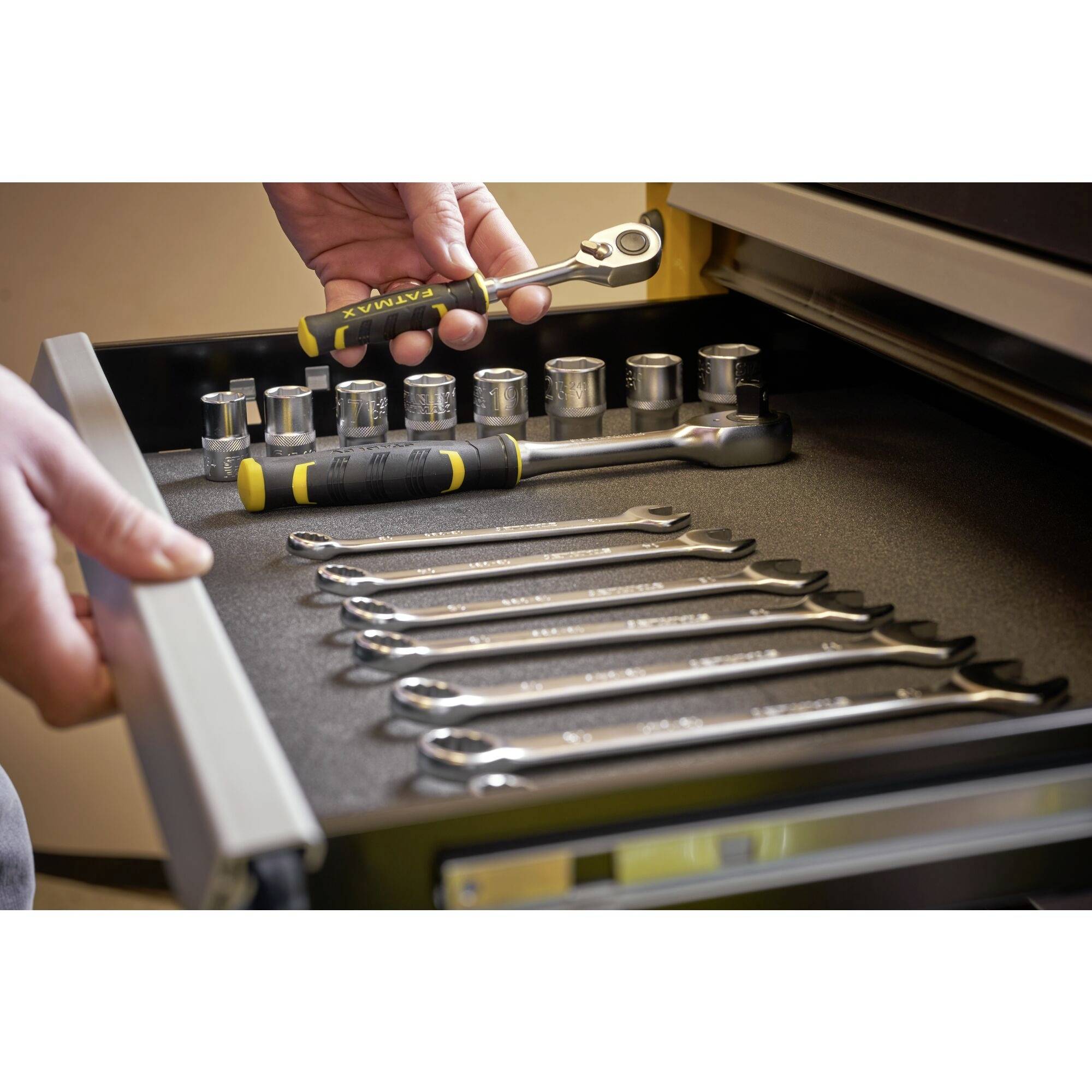 A person is organising a tool set in a drawer, including spanners and sockets, in a workshop environment.