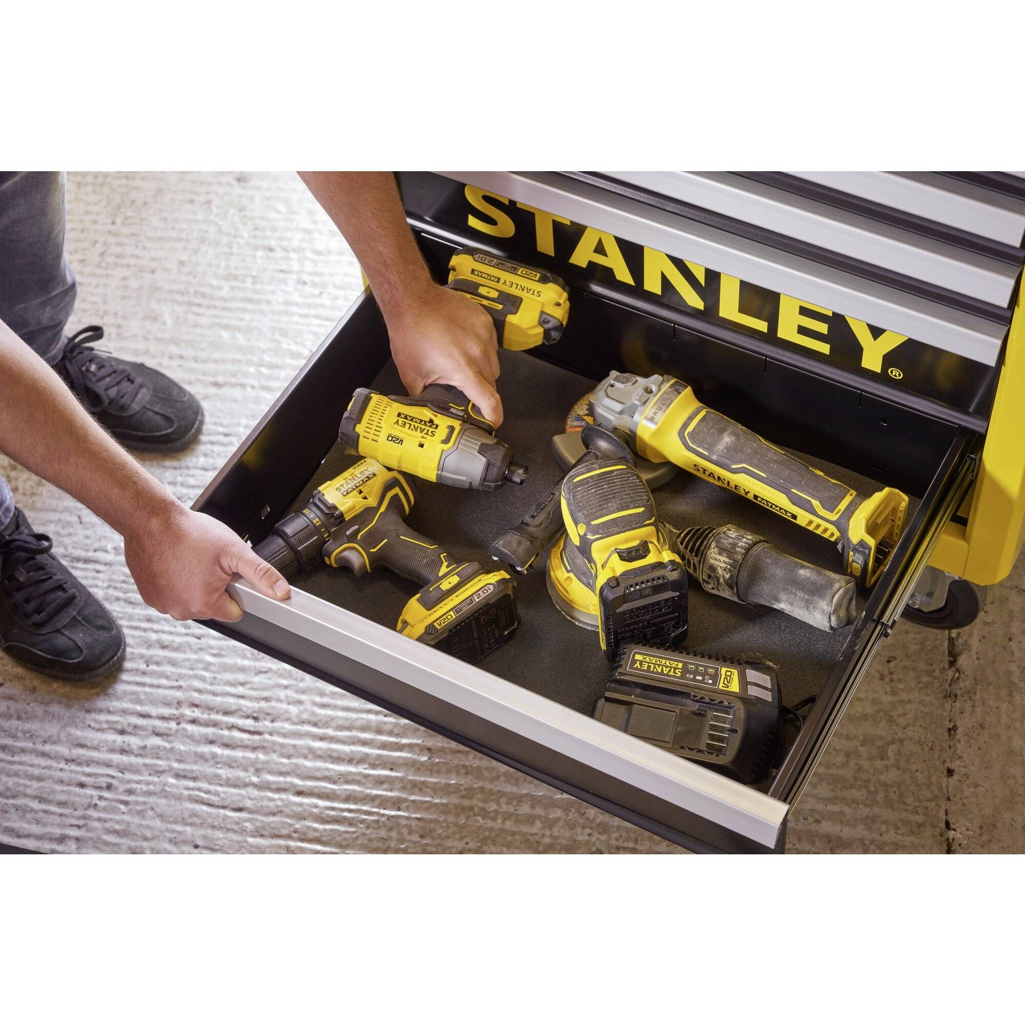 A person opens a drawer of a workshop trolley containing several yellow Stanley electric tools on a grey floor.