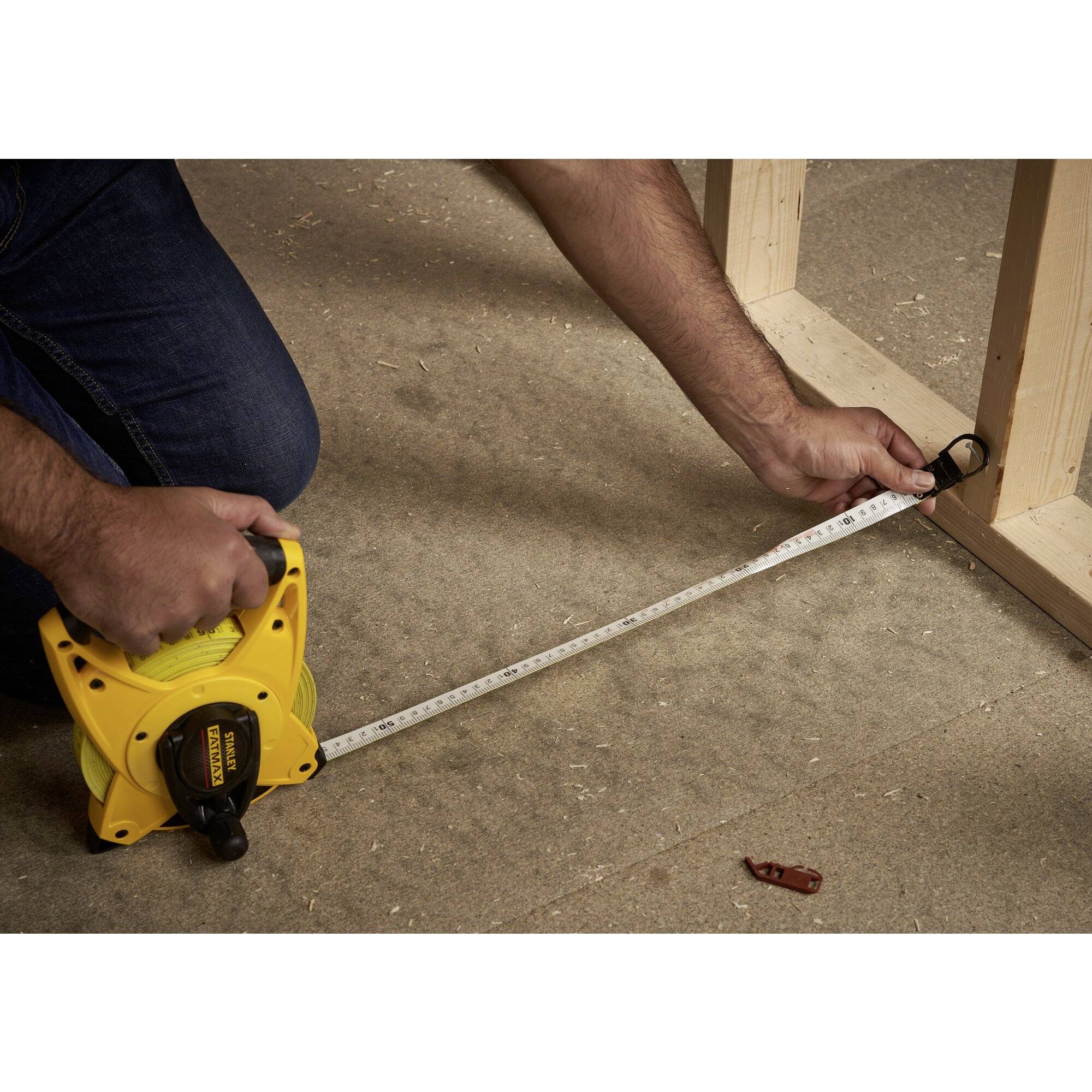 A person is measuring the distance with a yellow tape measure from a wooden edge on a floor covering.