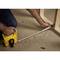 A person is measuring the distance with a yellow tape measure from a wooden edge on a floor covering.