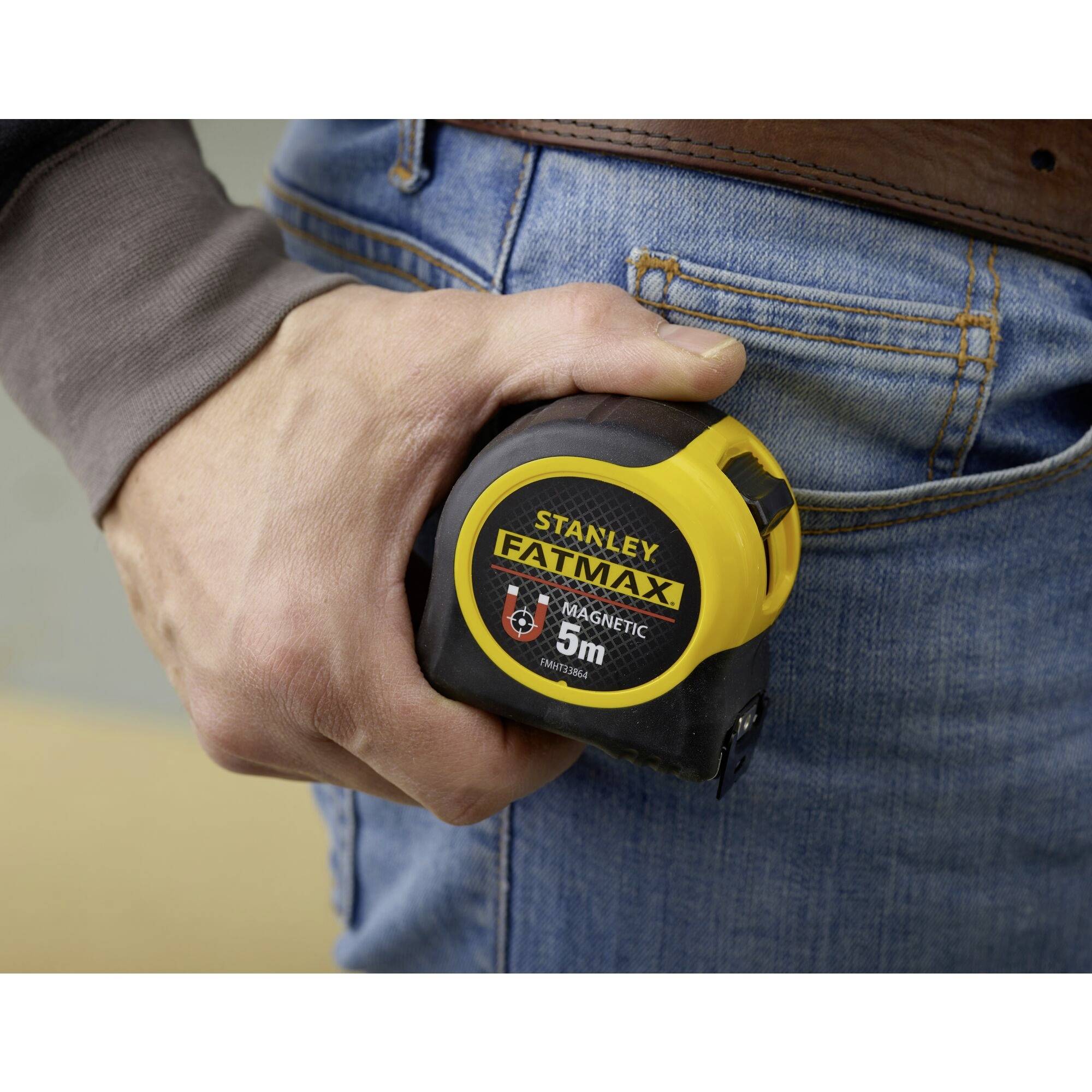 A person is holding a 5m Stanley FatMax tape measure with a yellow and black casing, which is clipped to their trouser waistband.