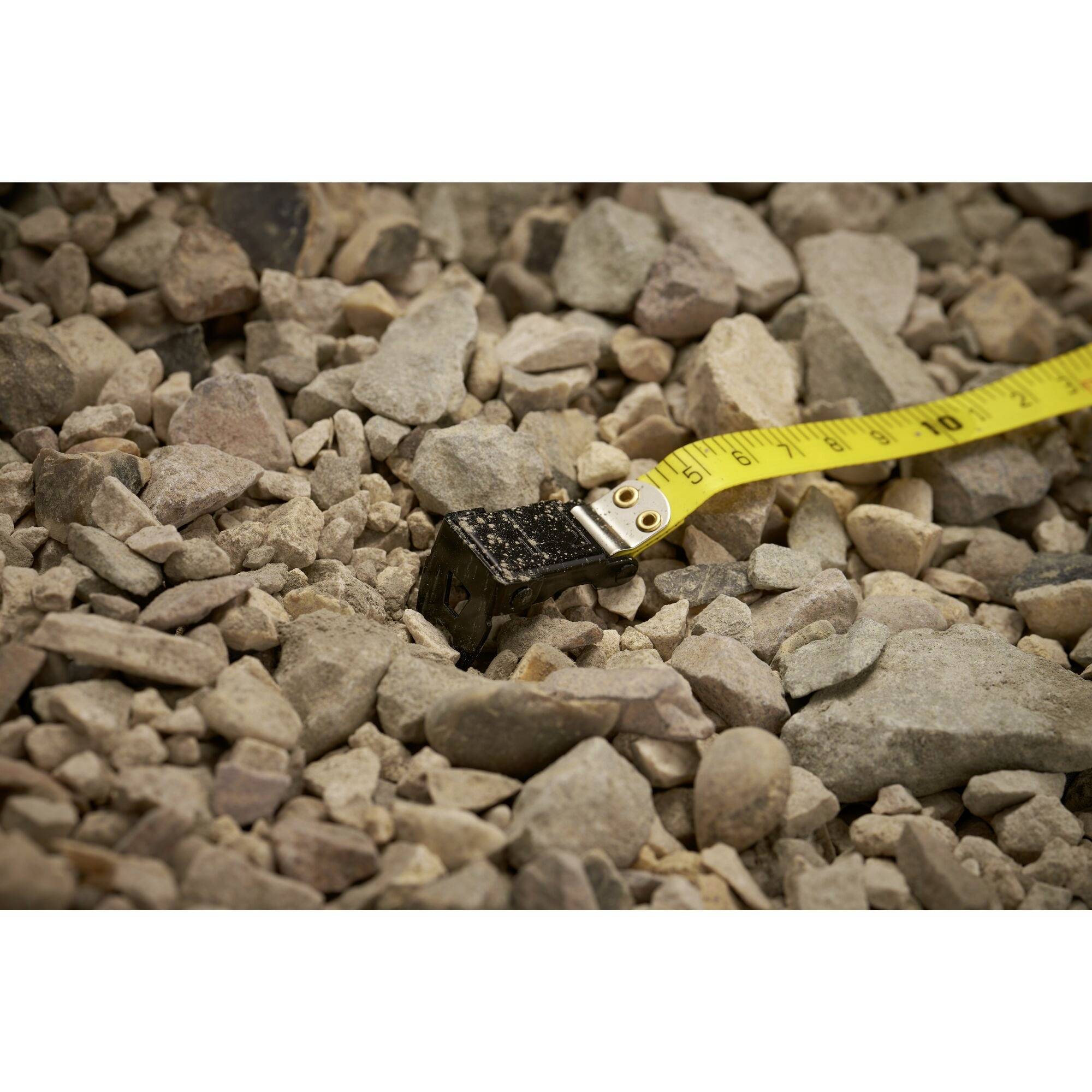 A tape measure lies on a pile of coarse, irregularly shaped gravel. The background shows only more stones.