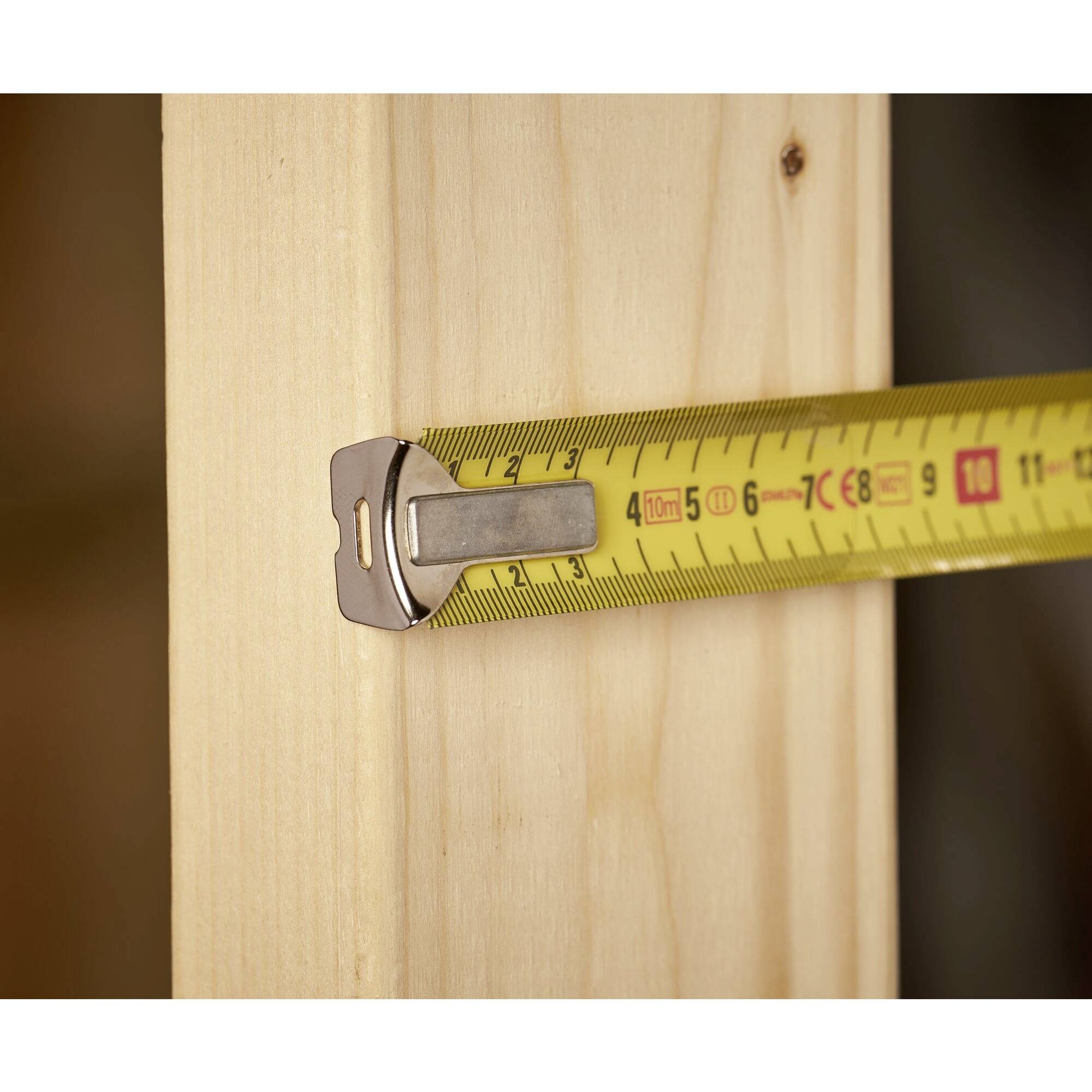 A yellow tape measure is placed against a wooden board. It shows a length of approximately 56 millimetres.