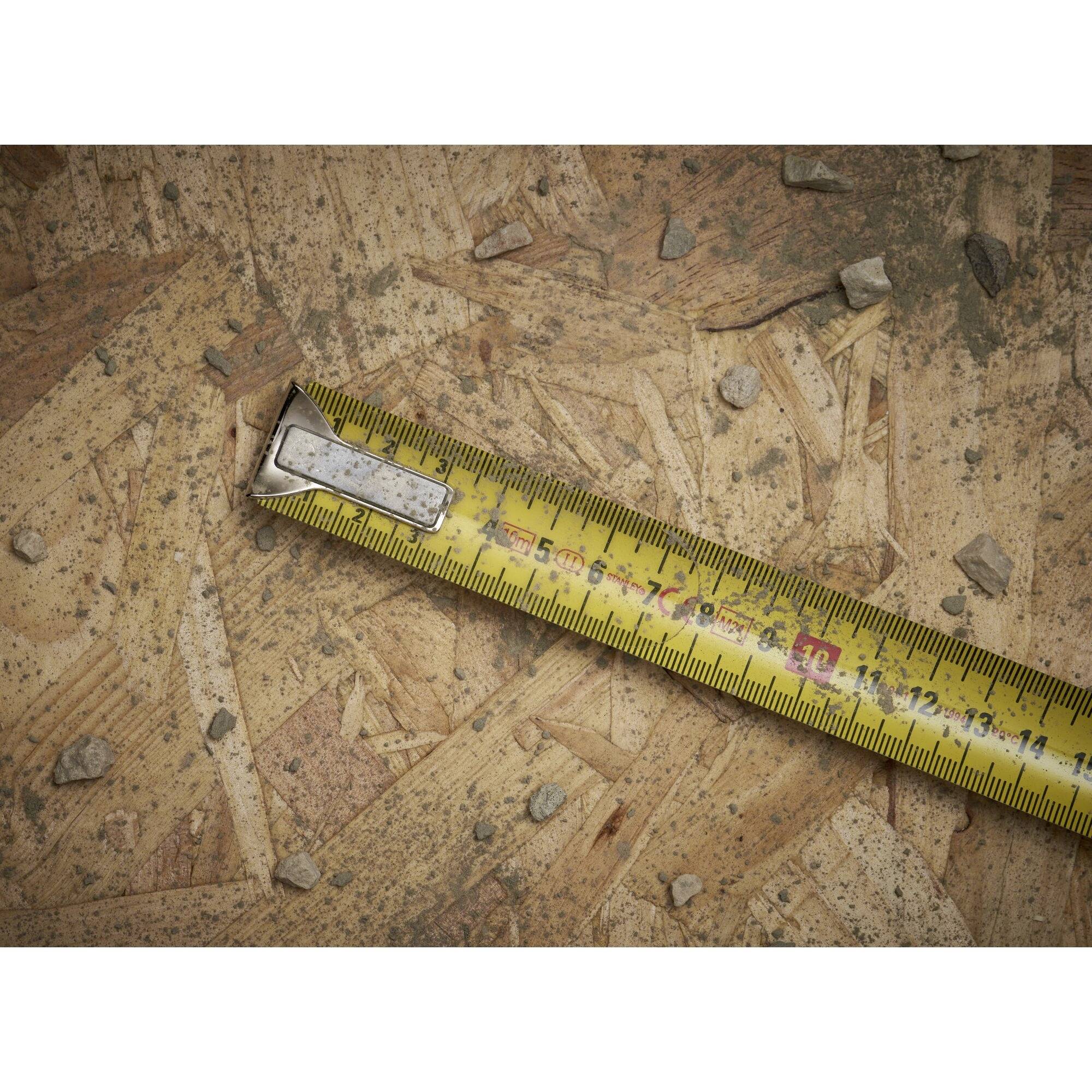 A yellow tape measure lies diagonally on a rough wooden surface with small stones.