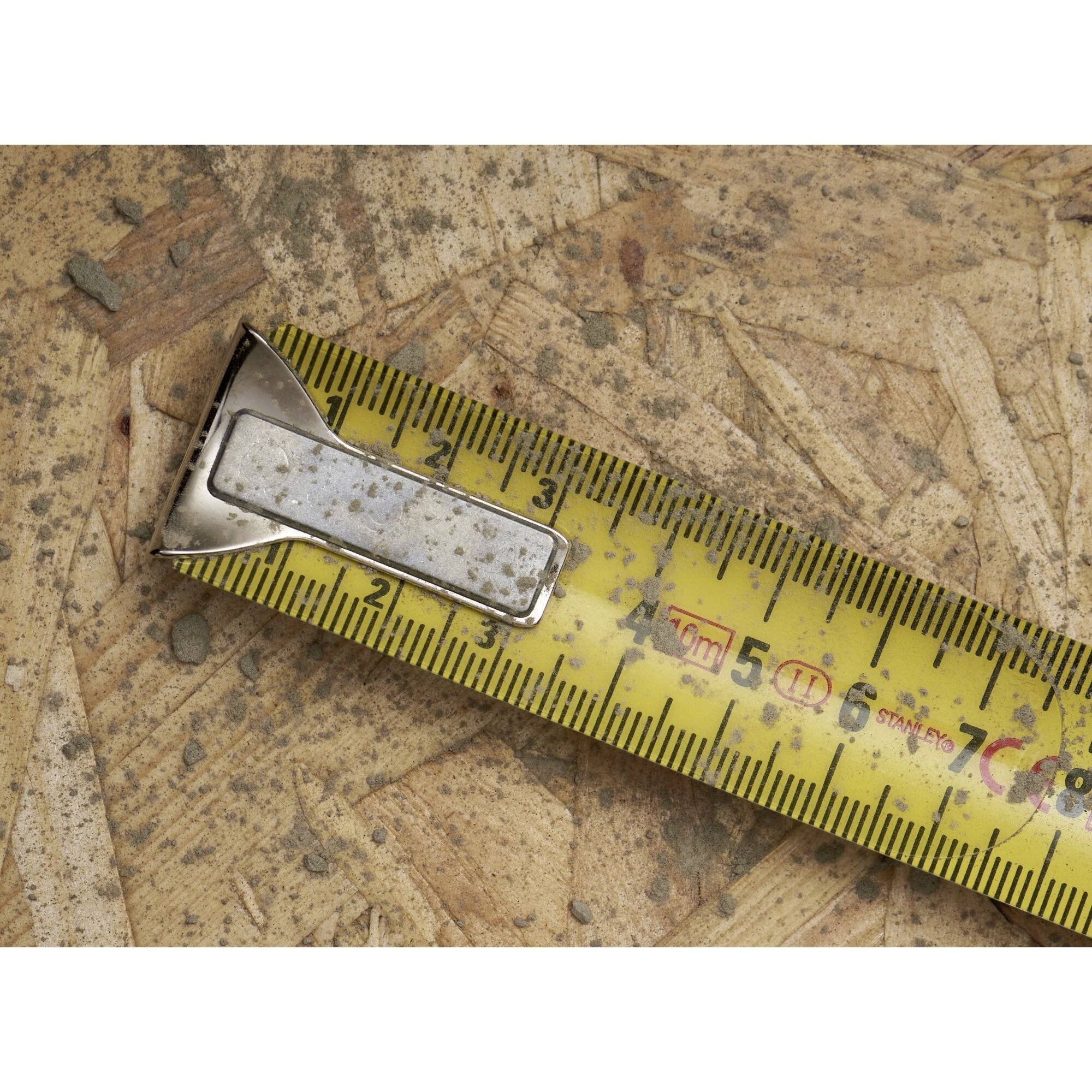 A tape measure lies on a wooden board. The yellow scale shows centimetres and inches.