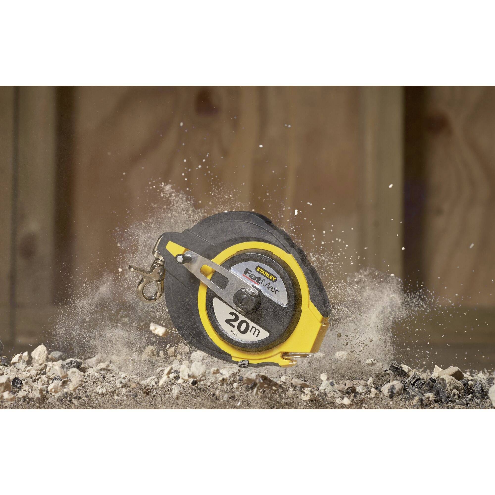 A yellow tape measure lies on dusty ground, surrounded by swirling dust and debris. Printed marking: 20 m.