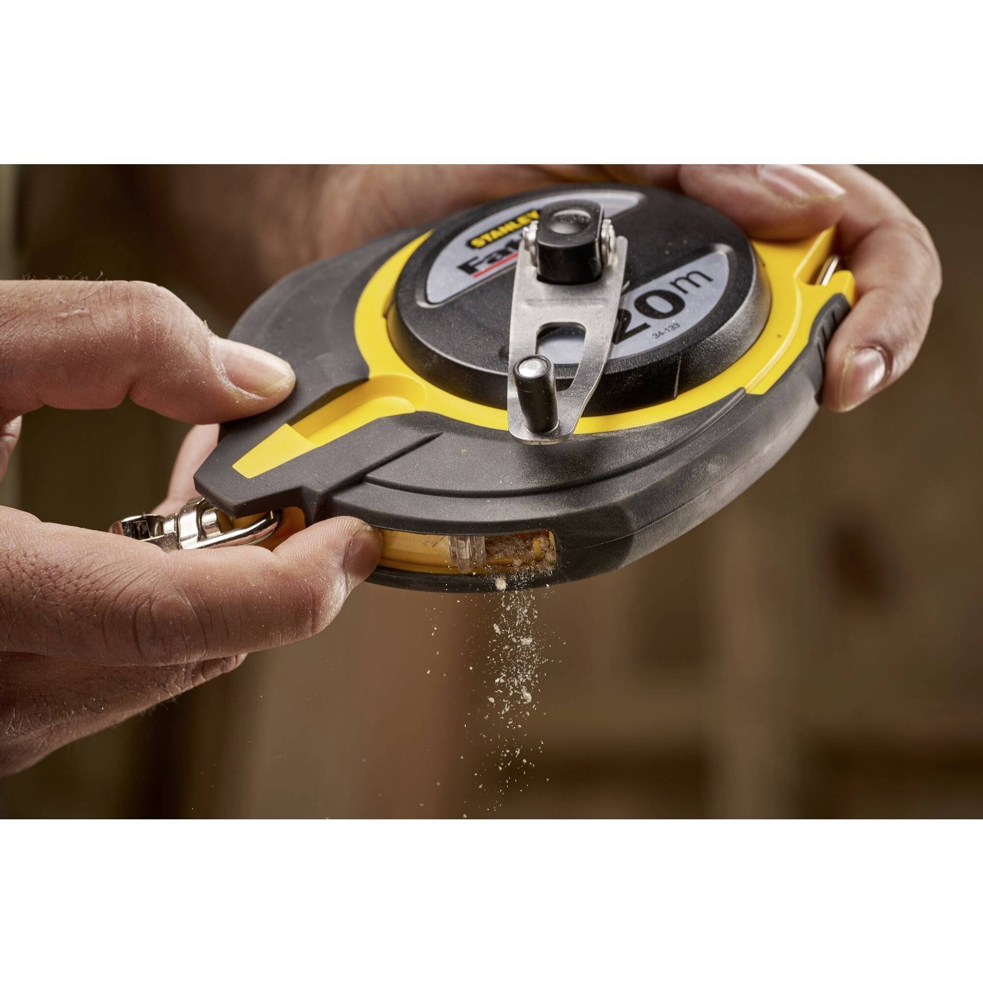 A person is holding a tape measure with a yellow and black casing and sprinkling chalk powder onto a surface to mark it.