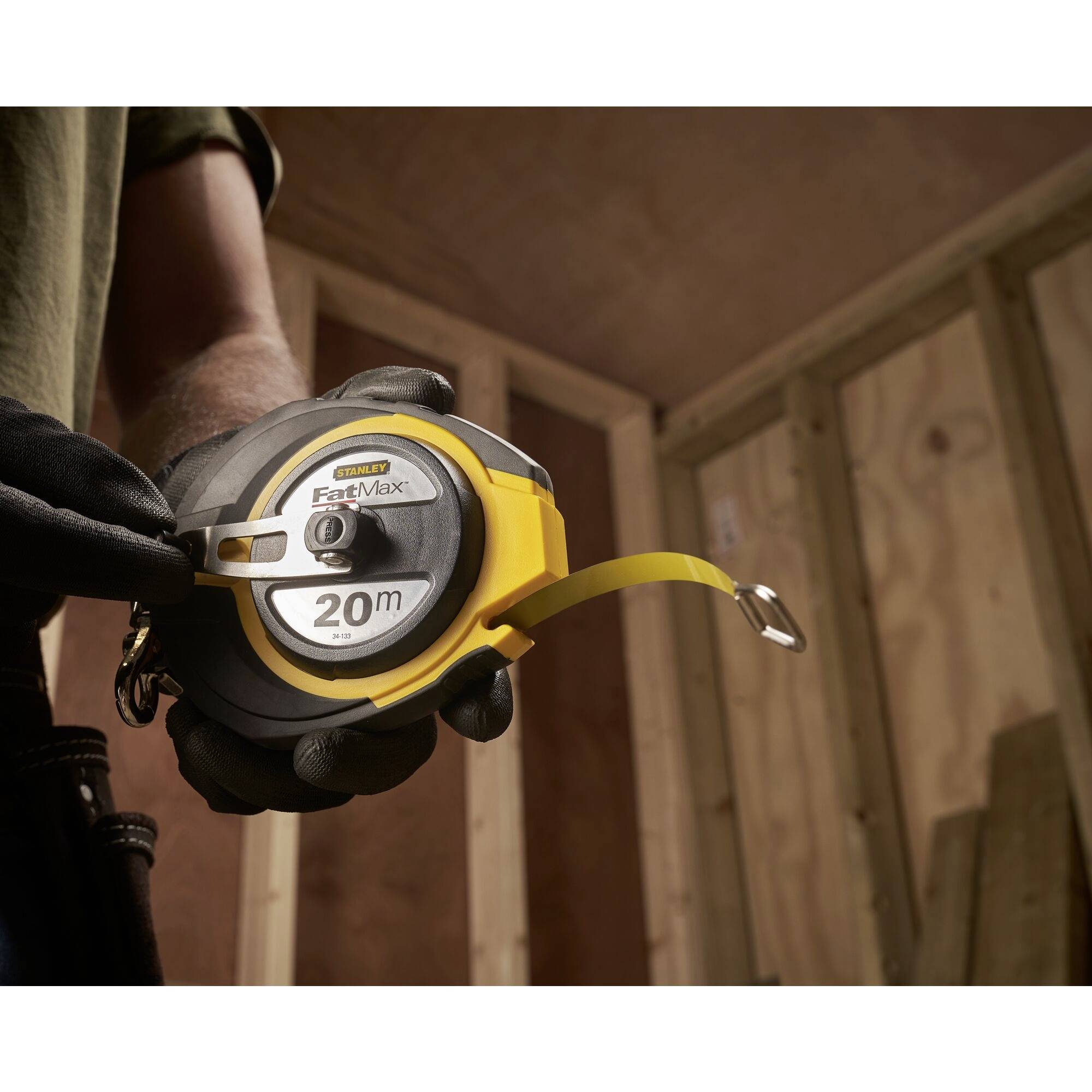 A person is holding a yellow measuring tape with the inscription '20 m' in a room under construction. The measuring tape is being unrolled.