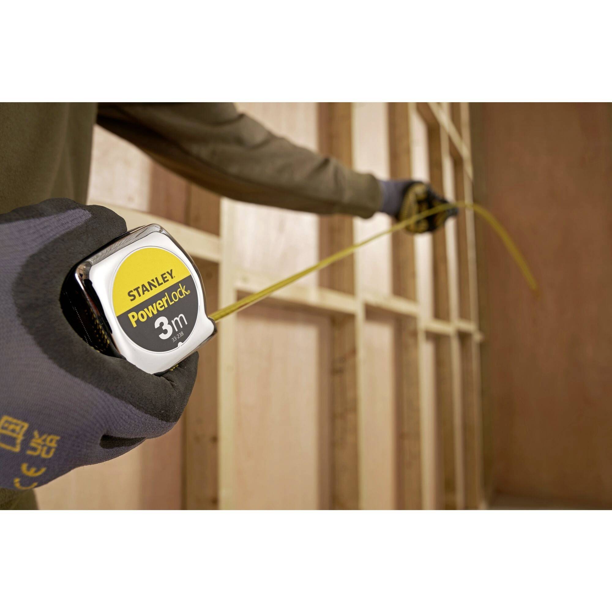 A person is measuring a wooden construction with a Stanley PowerLock 3m tape measure.