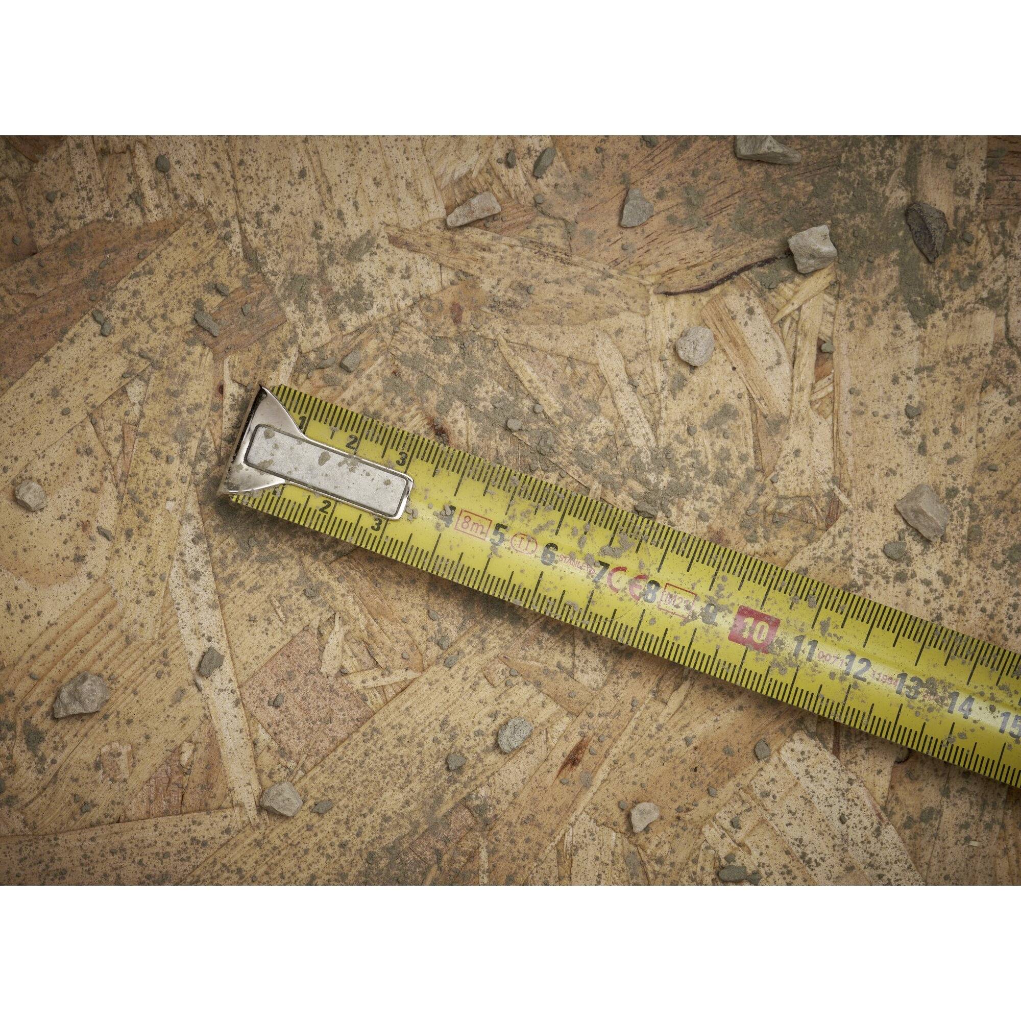 A yellow measuring tape lies on a wooden board with small stones scattered across it.