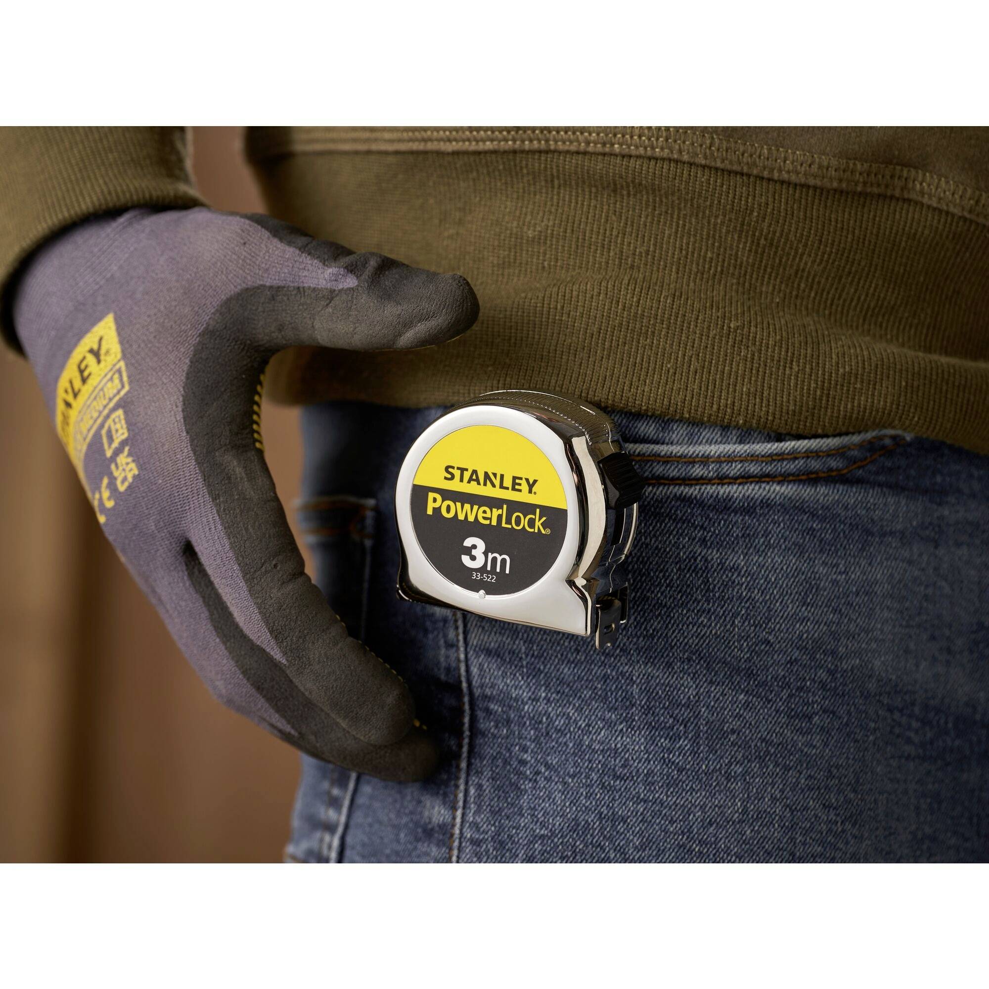 A Stanley PowerLock 3m folding ruler attached to a belt. A person wearing a work glove with the 'Stanley' logo.
