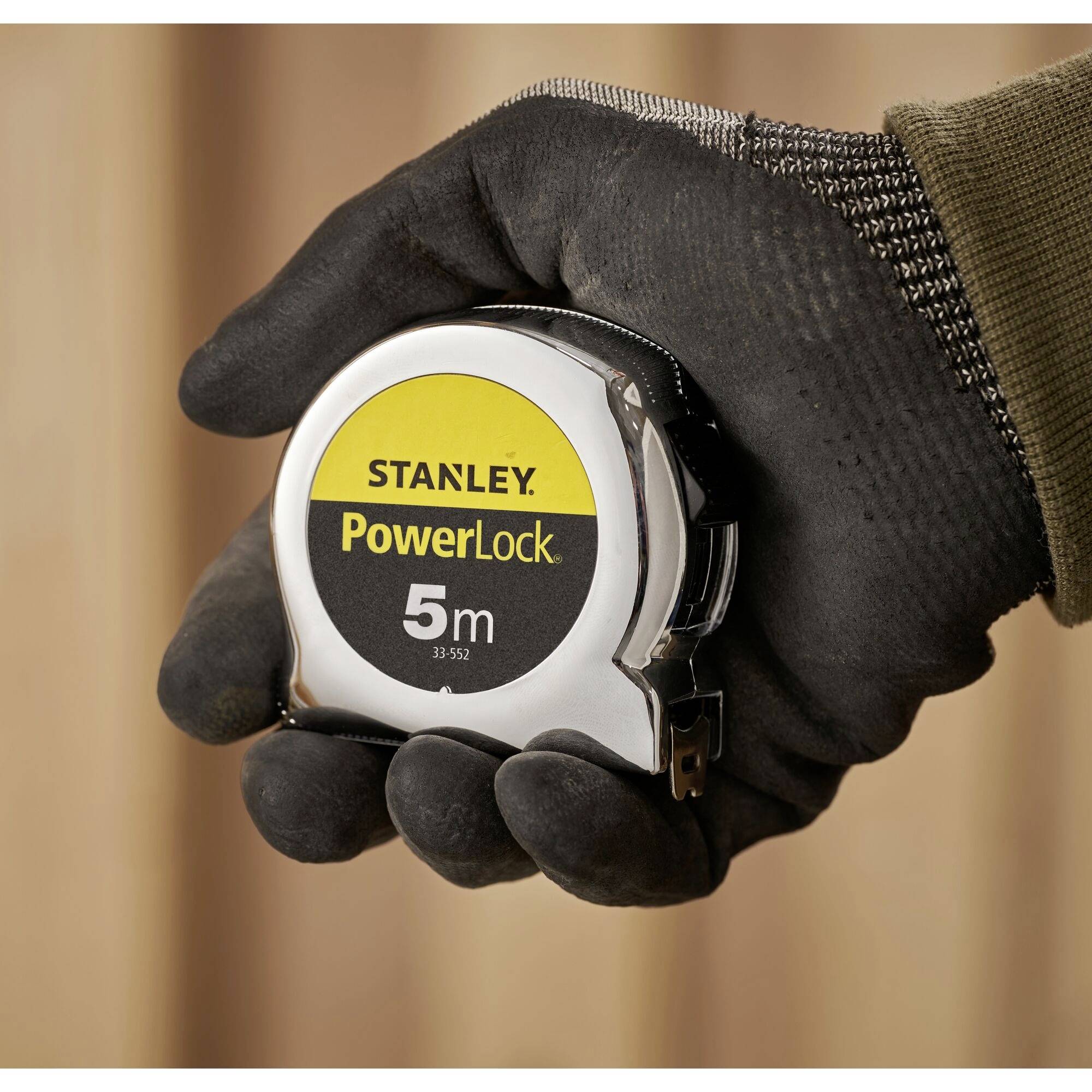 A gloved hand is holding a Stanley PowerLock 5-metre measuring tape.