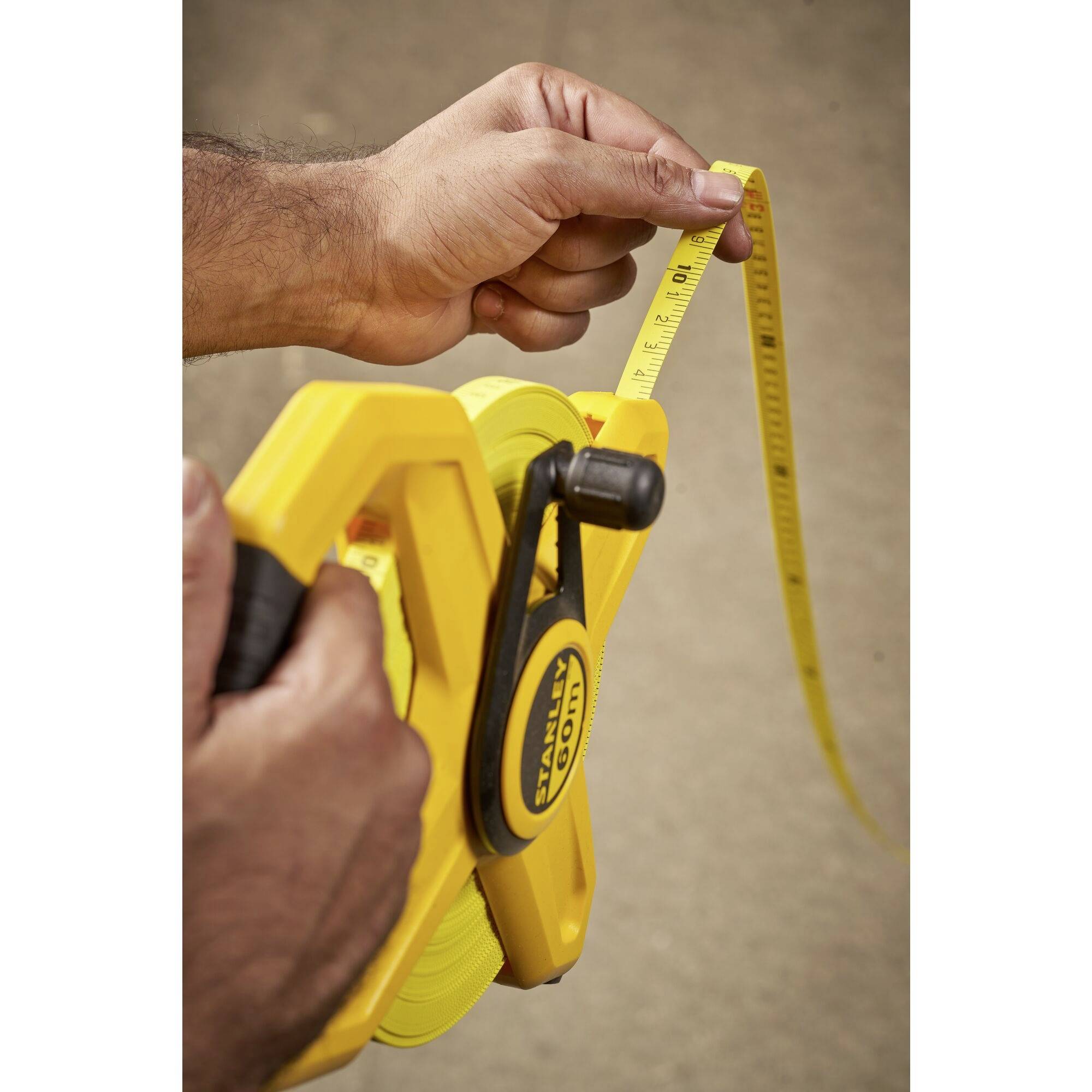 A person is holding a yellow measuring tape and measuring a length. Hands are showing the measurement on a stable surface.