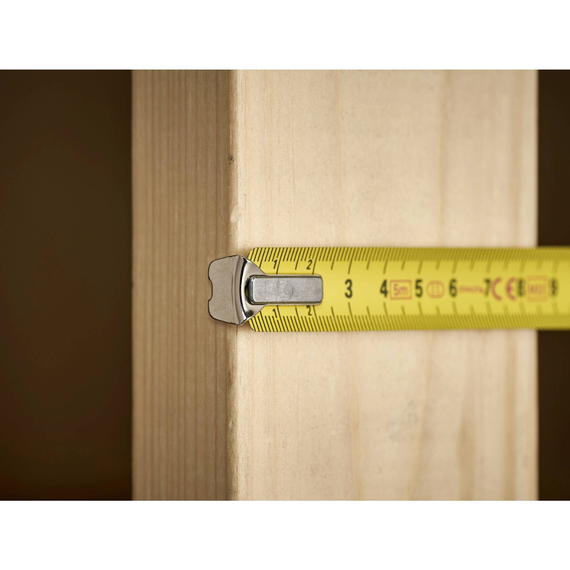 A yellow measuring tape is measuring the width of a wooden board.