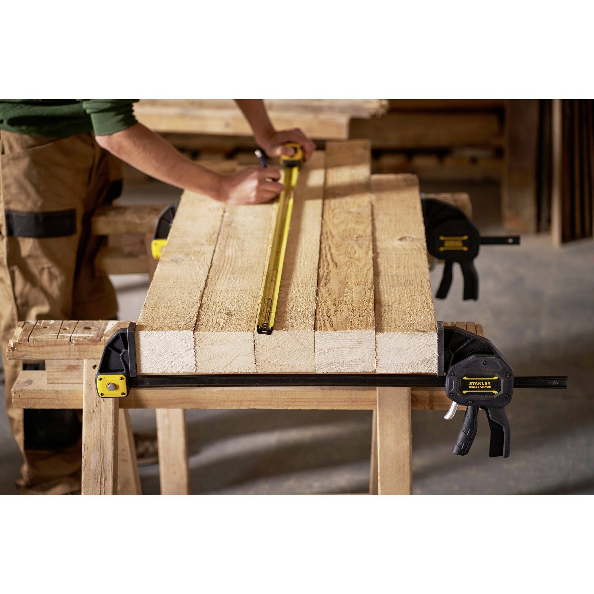 A person is measuring the length of wooden boards with a tape measure, which are secured to a workbench with clamps. Workplace in a workshop.