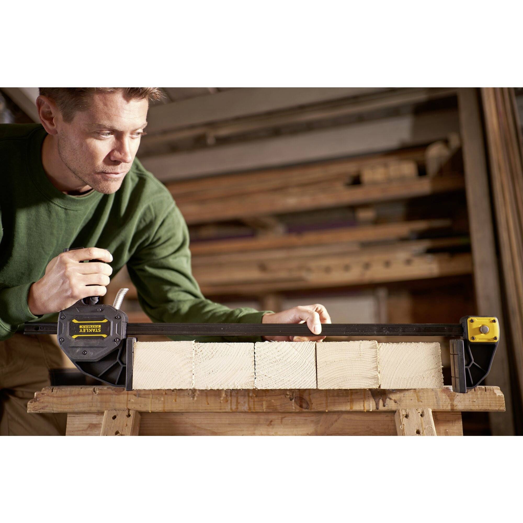 A man in a workshop is measuring the exact length of a wooden plank on a workbench using an electromagnetic device.