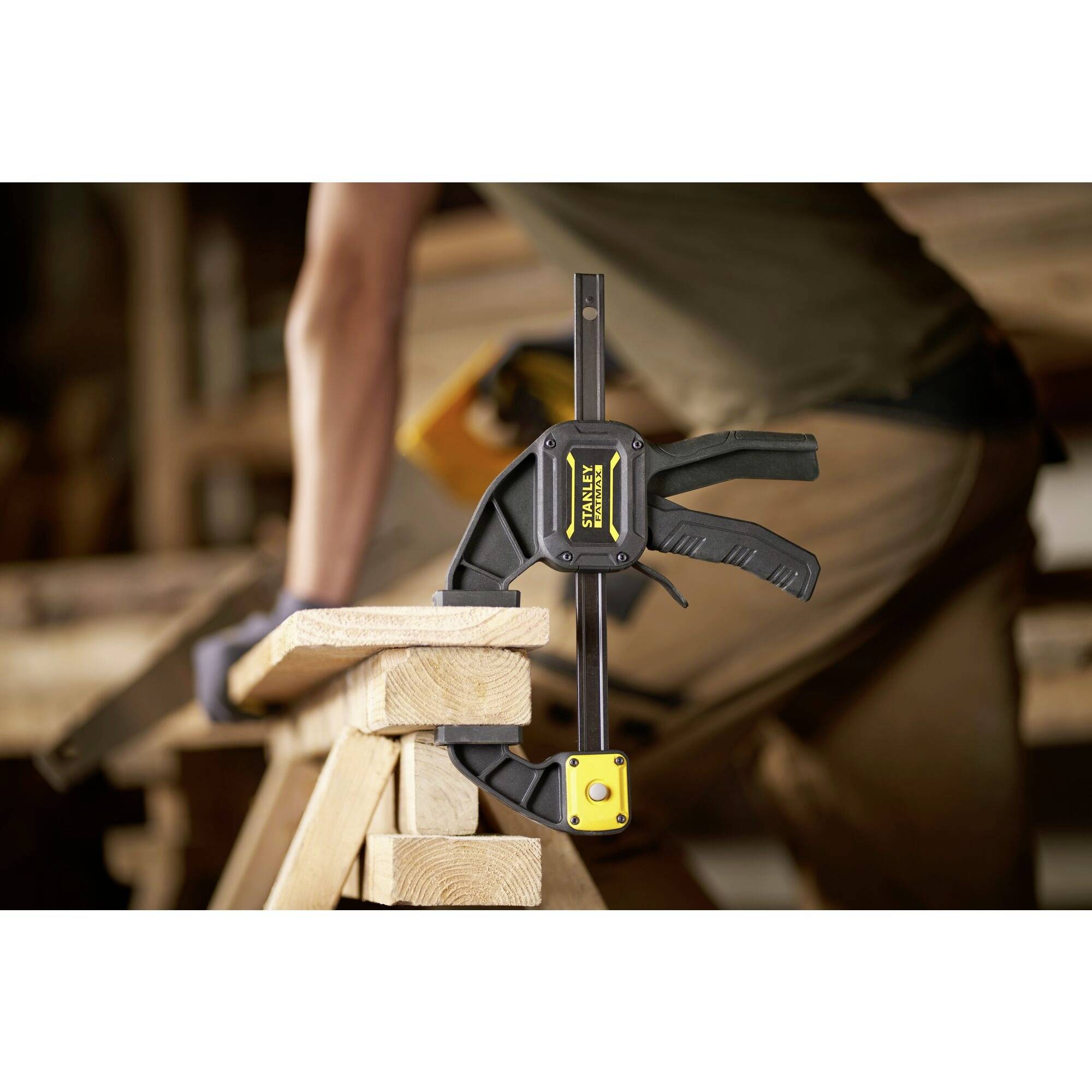 A person is using a clamp to secure wooden battens to a workbench in a workshop. Tools are visible in the background.