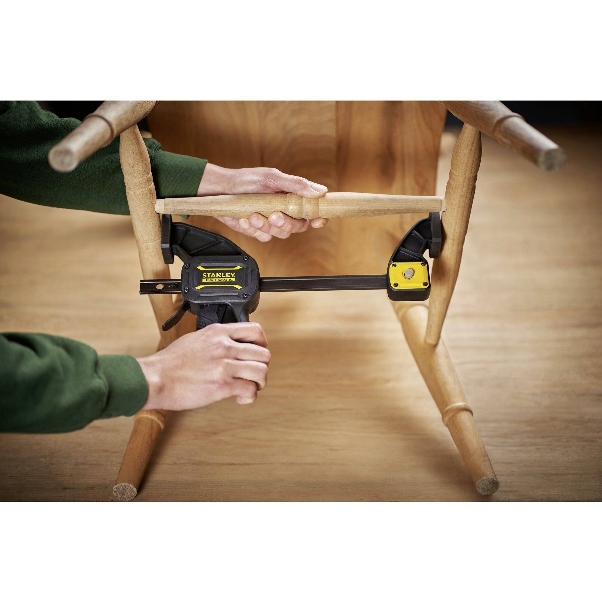 A person is using a G-clamp to secure a wooden piece to a wooden chair. The scene is taking place in a workshop.
