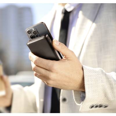 A person in a suit is holding two smartphones and a coffee cup. Blurred buildings can be seen in the background.