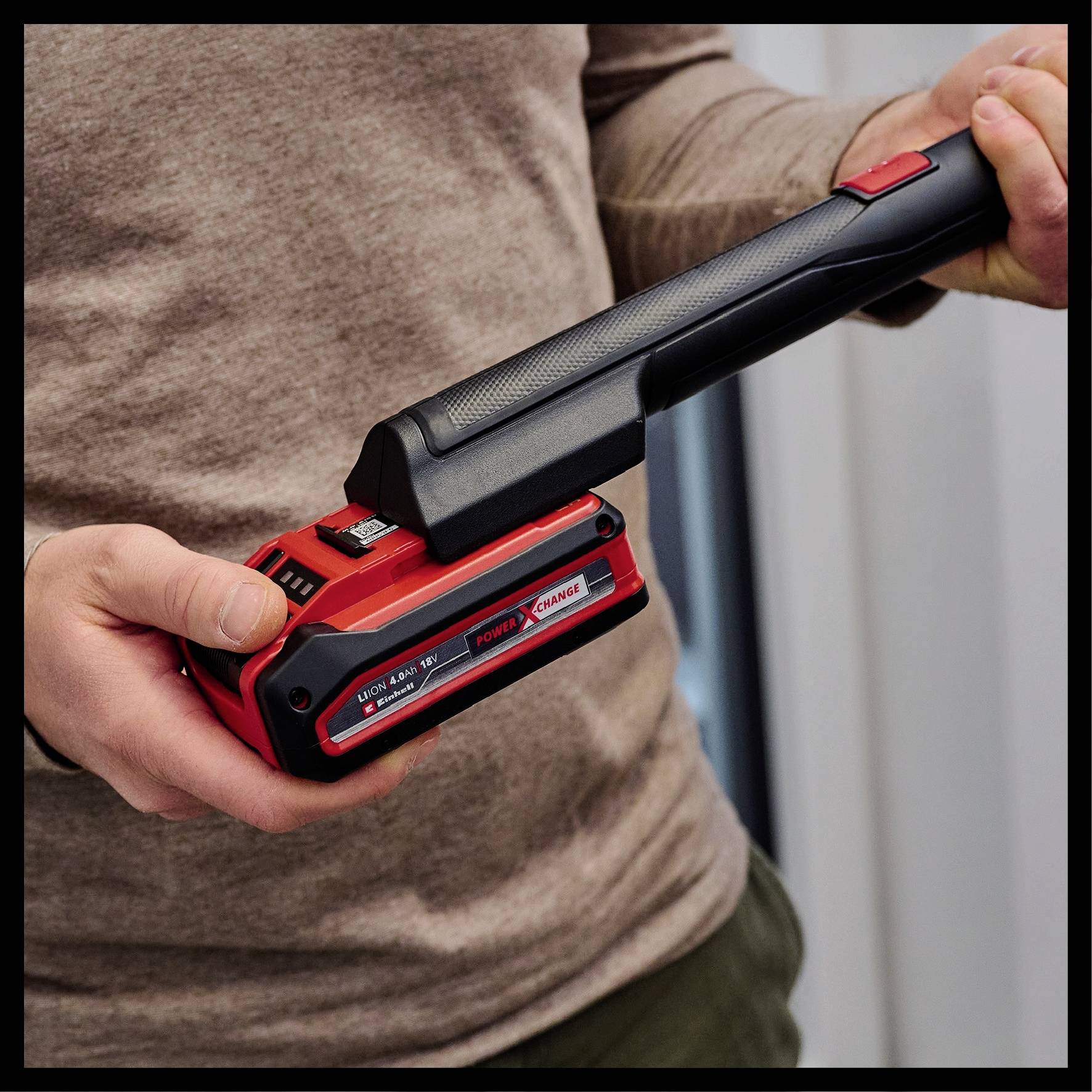 A person is holding an electric tool with a red handle and black casing, possibly used for DIY work.