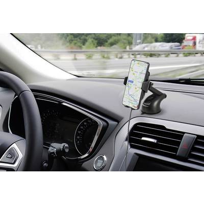 A smartphone with a navigation app is mounted in a holder on the dashboard of a car, with a road and green landscape in the background.