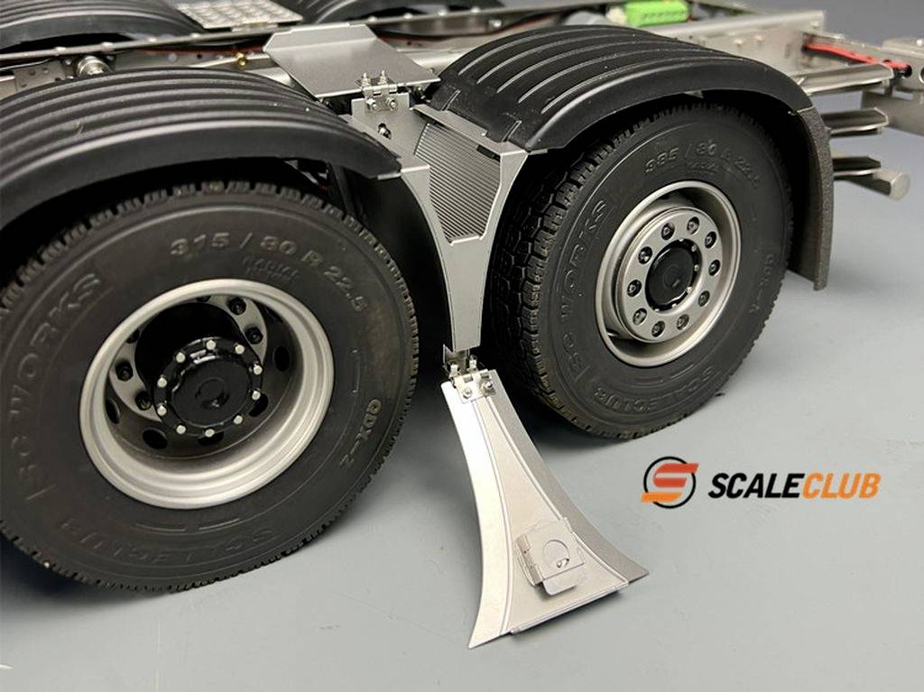 A model lorry with two rear wheels stands on a grey background. A metal stand is visible next to the wheels.