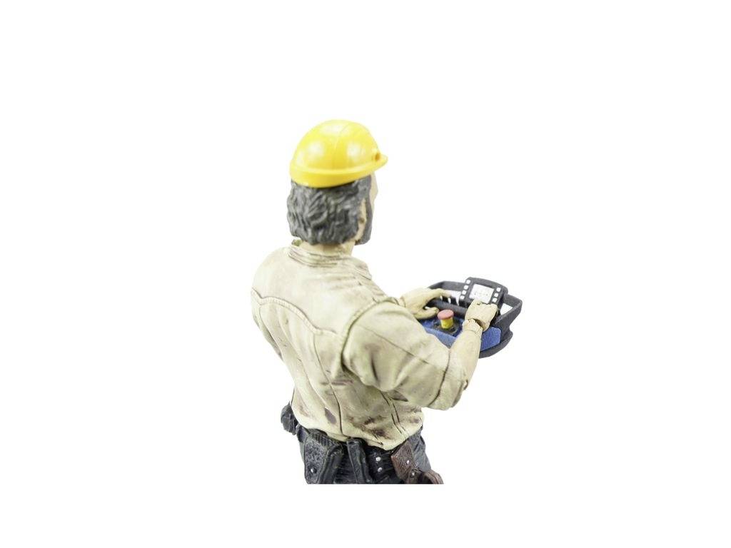 A construction worker wearing a yellow hard hat is operating a portable control panel and looking at it.