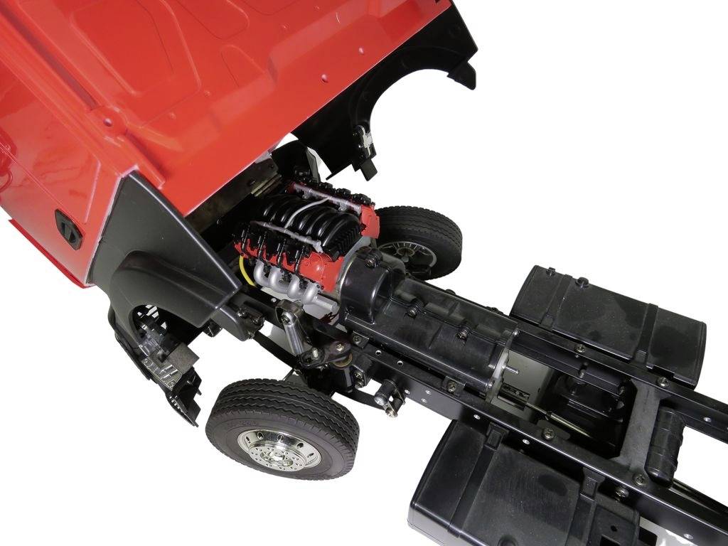 A red lorry cabin with an open bonnet reveals the exposed engine and chassis, including front axles and wheels.