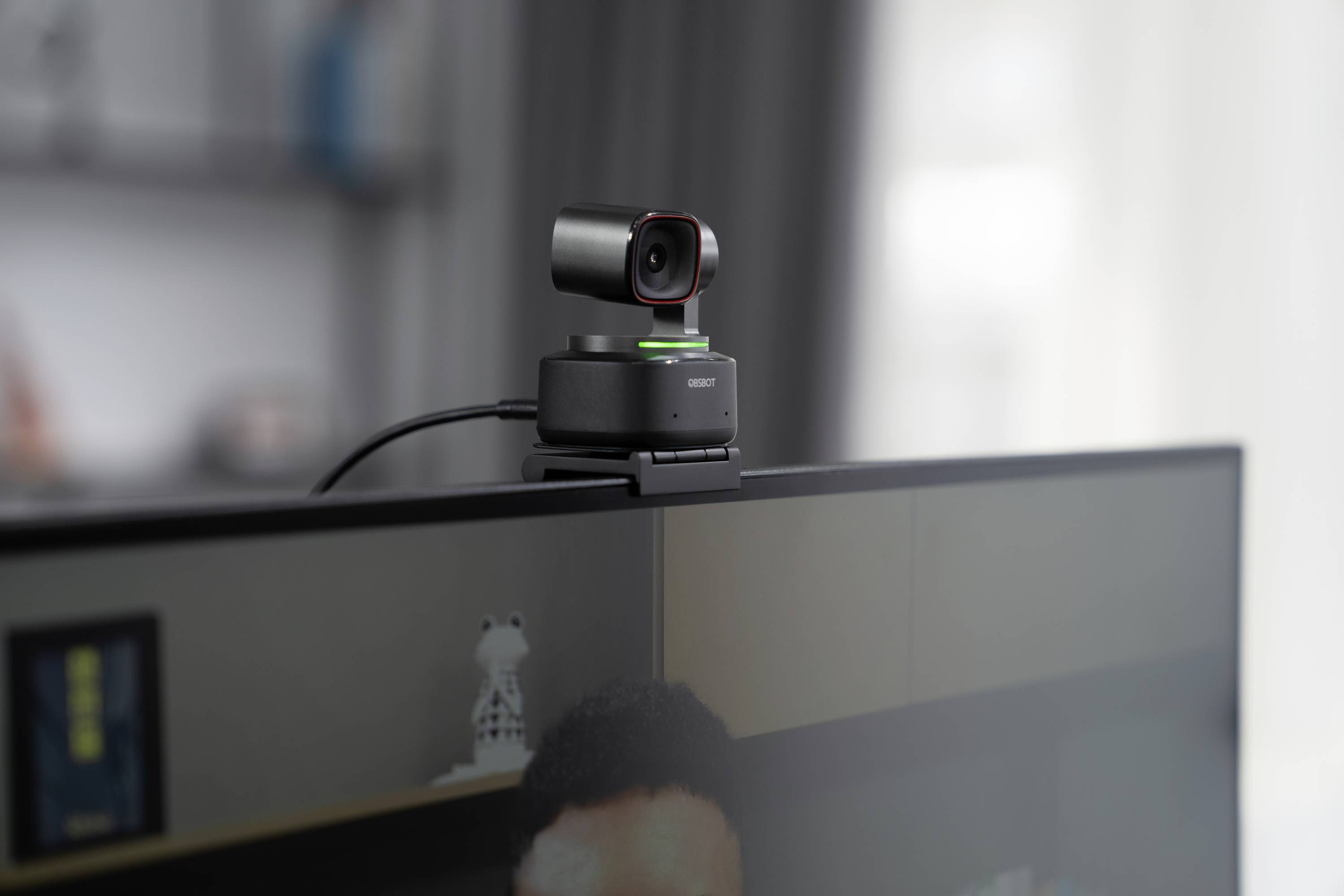 A webcam is mounted on a monitor. A blurry bookshelf can be seen in the background.