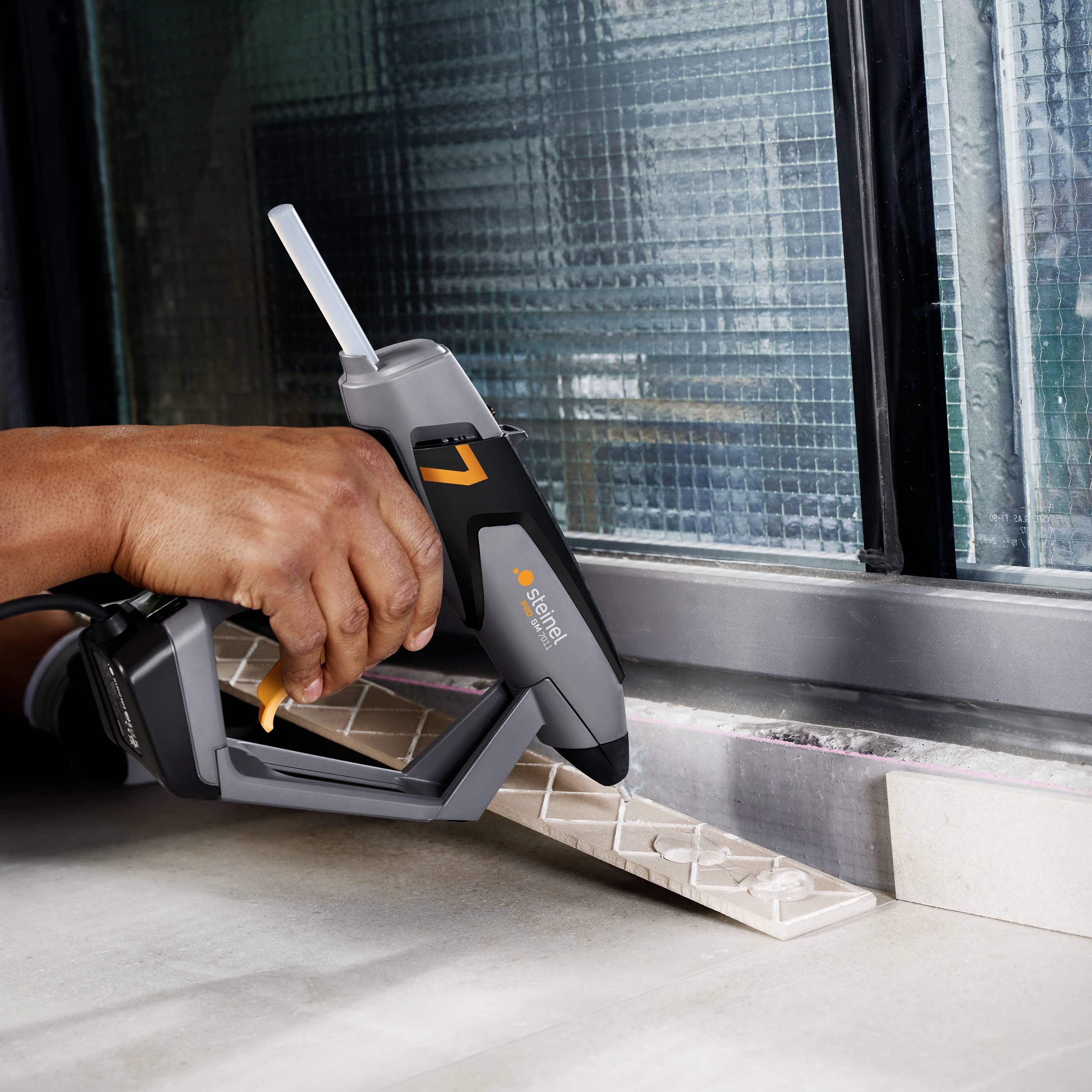 A person is using a black silicon gun to seal a joint around a window frame. The window is made of glass blocks.