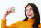 Woman in an orange jumper holding a round digital thermometer and hygrometer, showing 25.6°C and 70% humidity, smiling.