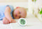 A sleeping baby in the background; in the foreground a digital thermo-hygrometer displaying 25°C and 70% relative humidity.