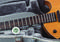An acoustic guitar lies in an open case lined with velvet. A hygrometer indicates a temperature of 25.6°C and 70% humidity.