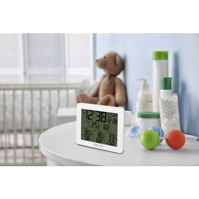 A table in a children's bedroom with bathing items, toys and a digital thermometer displaying temperature and humidity. A blurred teddy bear in the background.