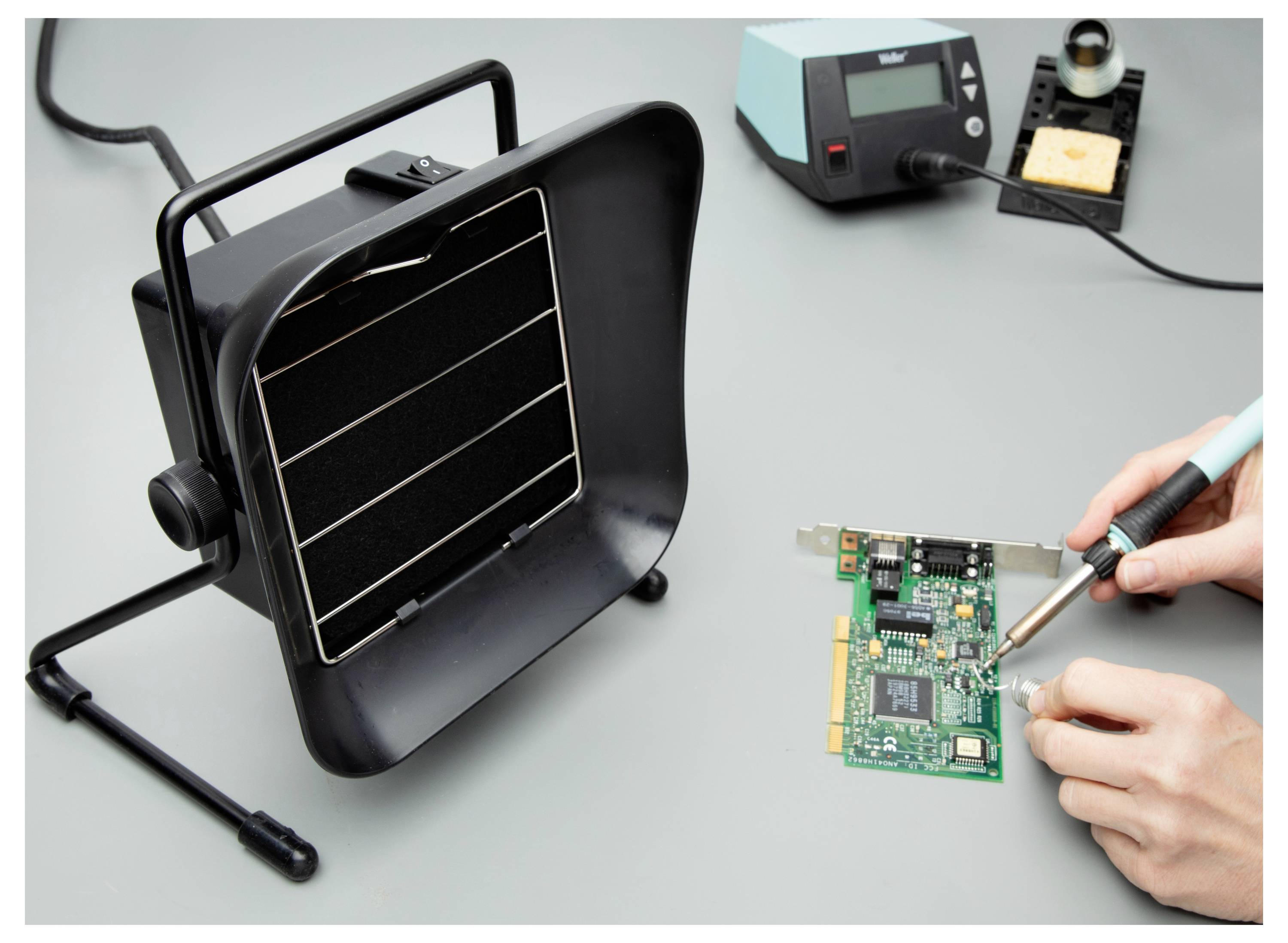 'A person is soldering a circuit board with a soldering iron, using a fume extractor for safety. An electronic repair setup is shown.'