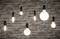 Various light bulbs hang in front of a brick wall. The shapes and sizes vary, some are illuminated, others are switched off.