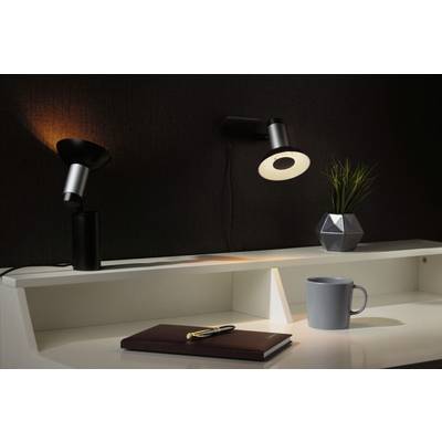 Two contemporary desk lamps on a white desk illuminate a notebook with a pen, a coffee cup and a plant in a geometric pot.