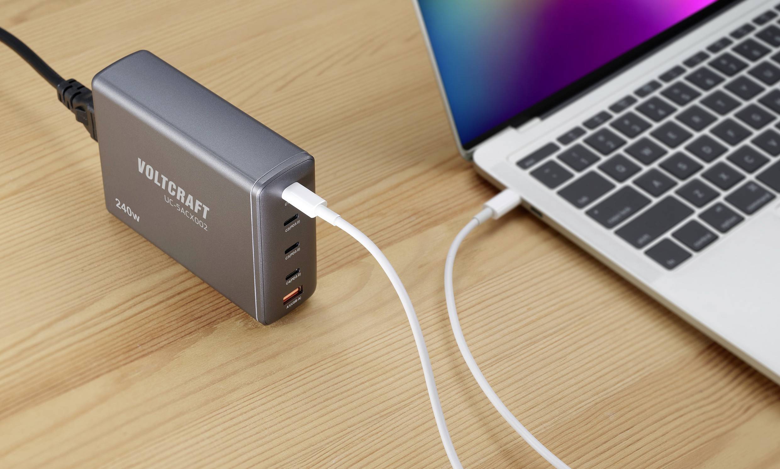 A laptop is being charged via a USB cable from a multi-plug charger on a wooden table.