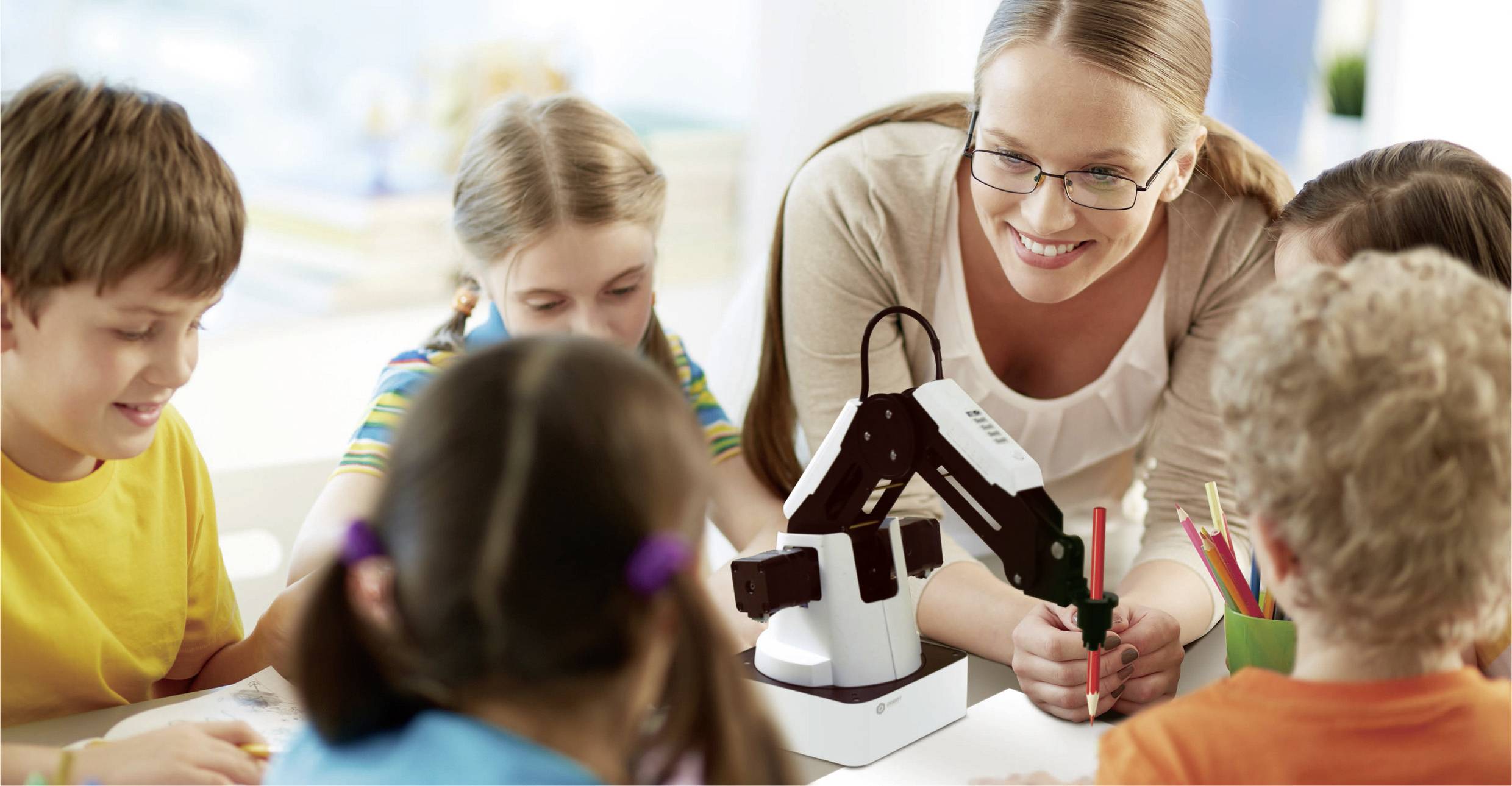 A teacher is showing a small robotic arm to five children. The children look intrigued and are concentrating on the demonstration.