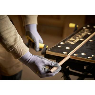 A person is holding and cutting a copper pipe with a pipe cutter. They are wearing gloves and working at a workbench.