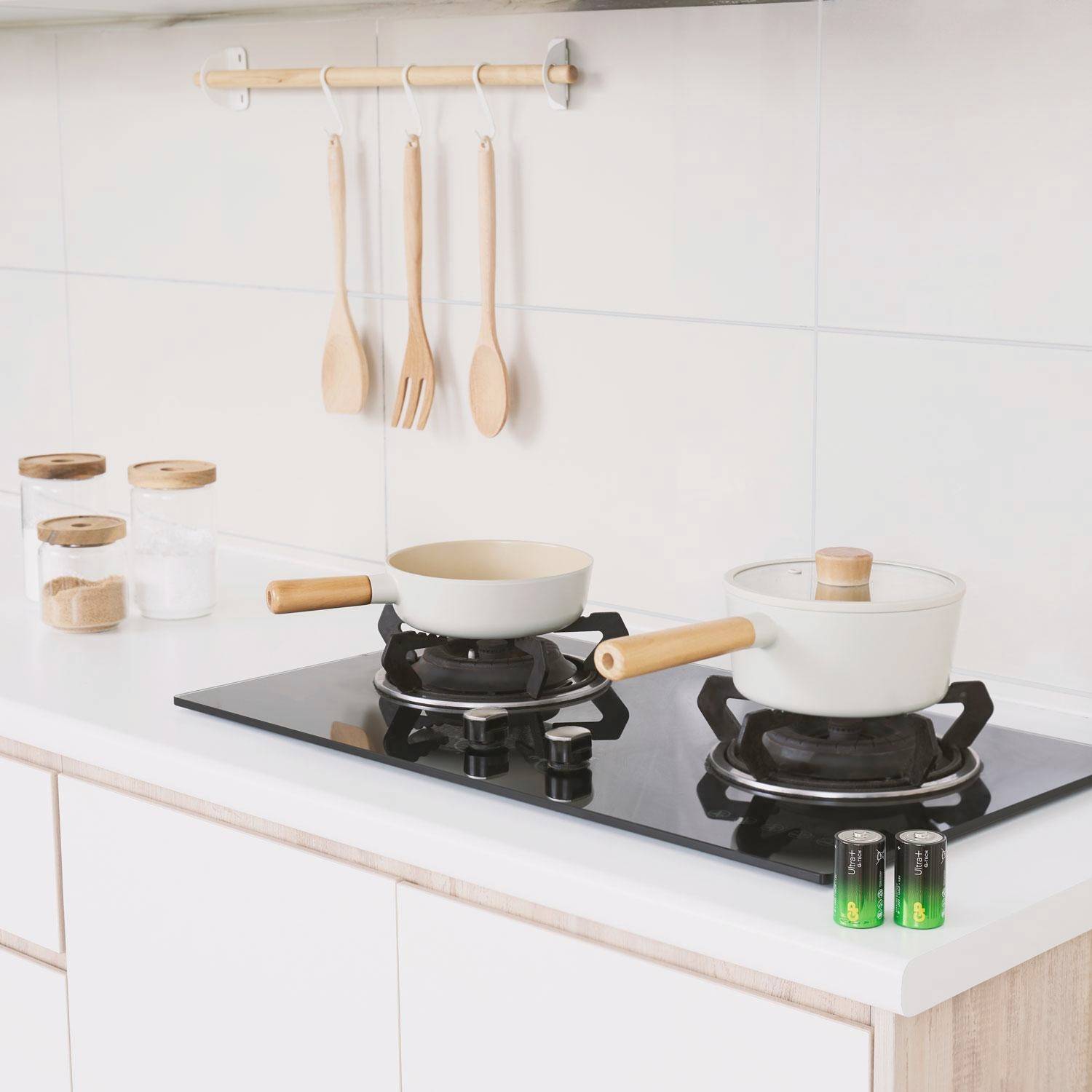 Bright, modern kitchen with two hob rings, pans on the stove, wooden spoons on the wall and storage jars on the worktop.