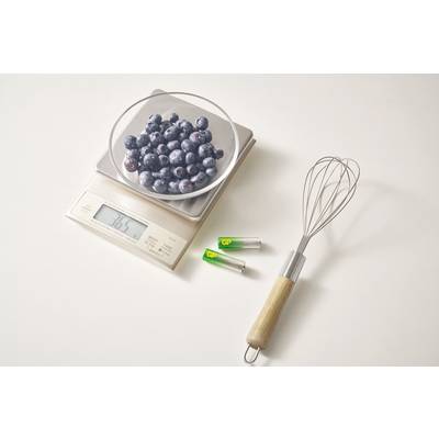 A bowl of blueberries sits on a kitchen scale, displaying 186.5 grams. Beside it are a whisk and two small test tubes.