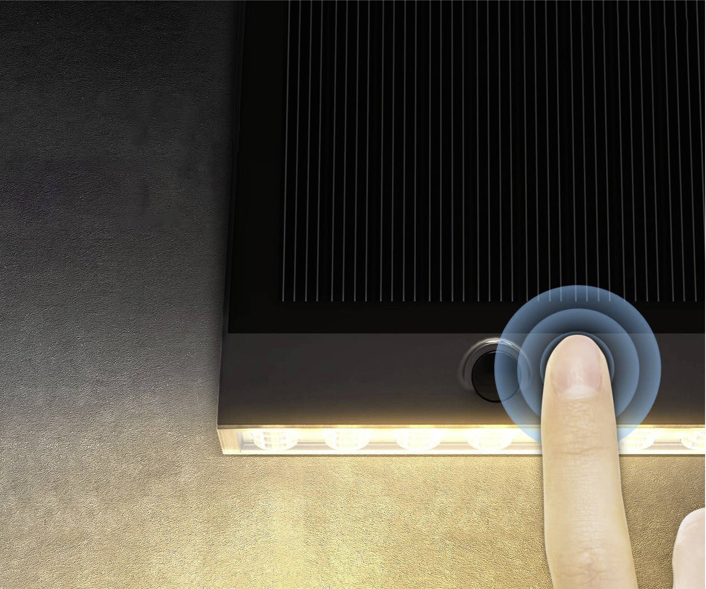 A finger touches the button of a solar lamp, which illuminates at its bottom edge, against a dark background.