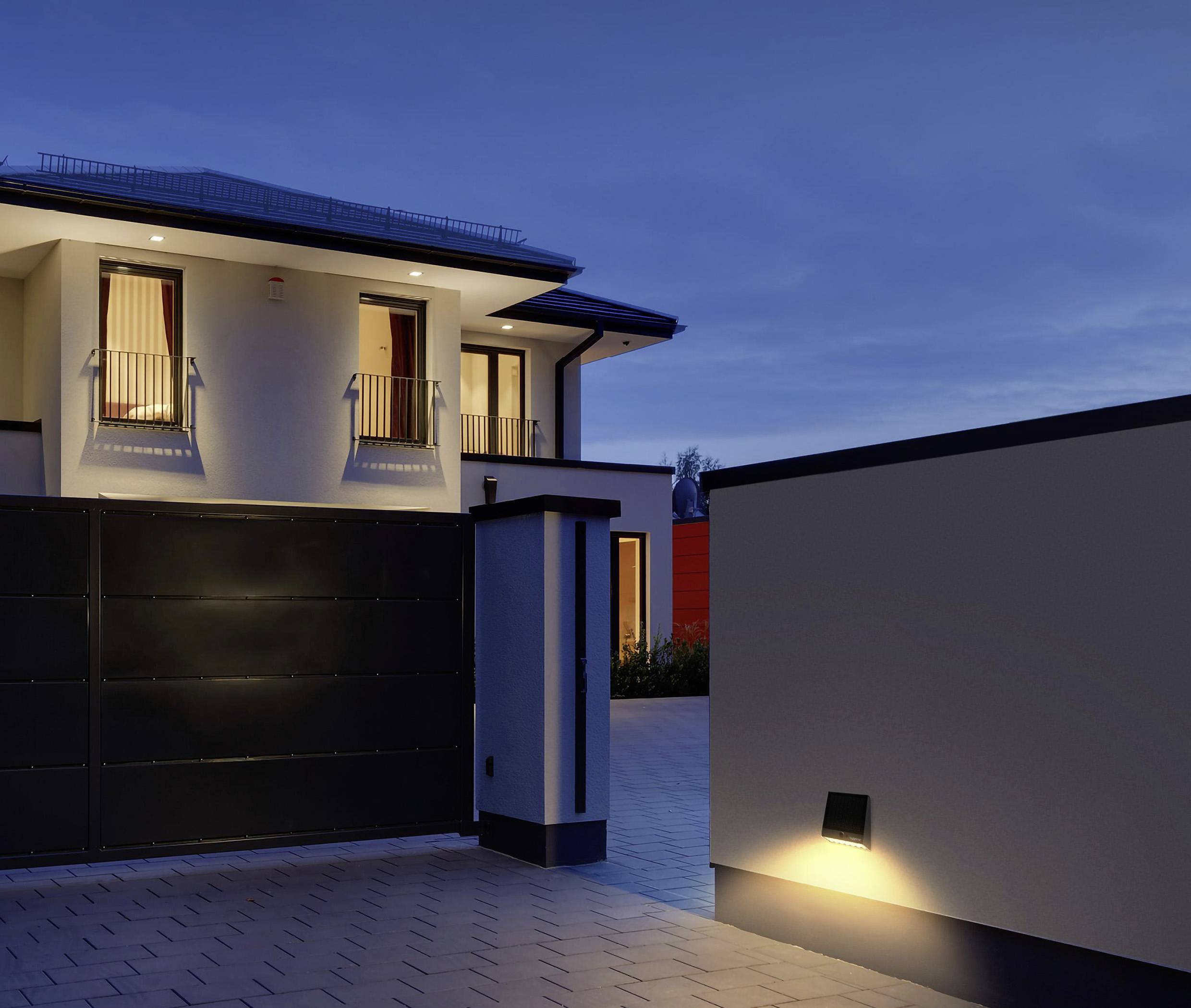 Two-storey house at dusk, illuminated windows and driveway gate. Modern architecture with clean lines.