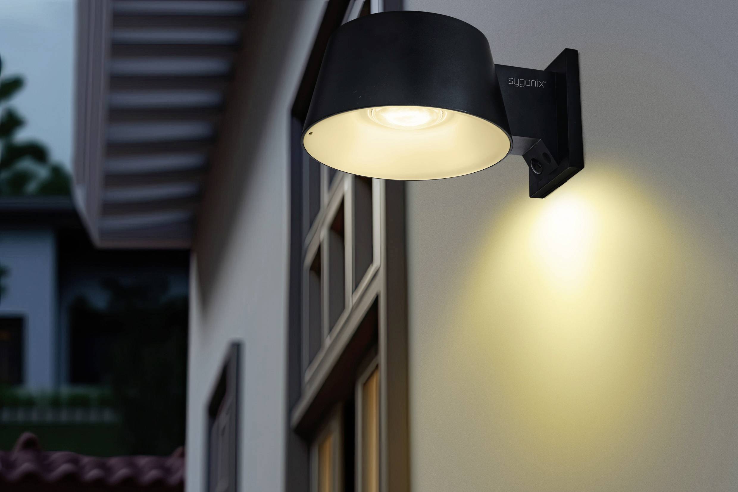 An exterior wall light illuminates a house wall at dusk, highlighting modern architectural details and creating a warm ambience.