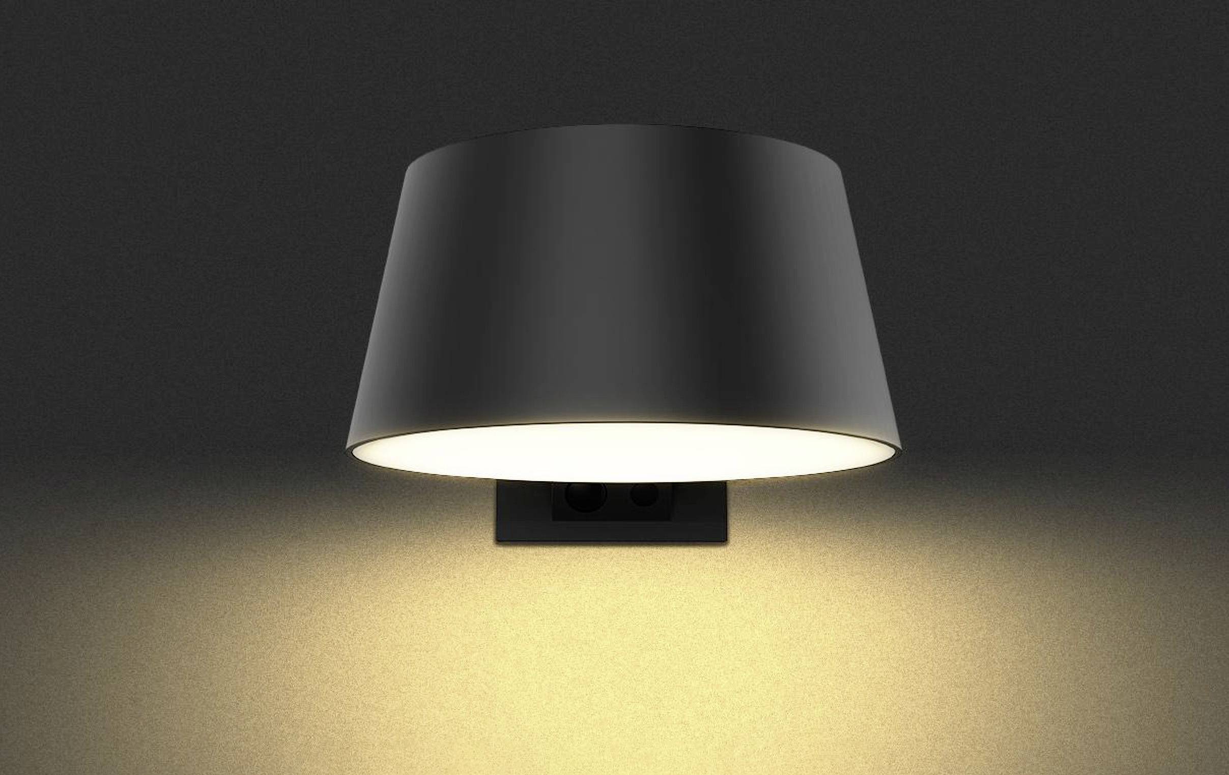Black wall light switched on, illuminating wall with warm light directed downwards.