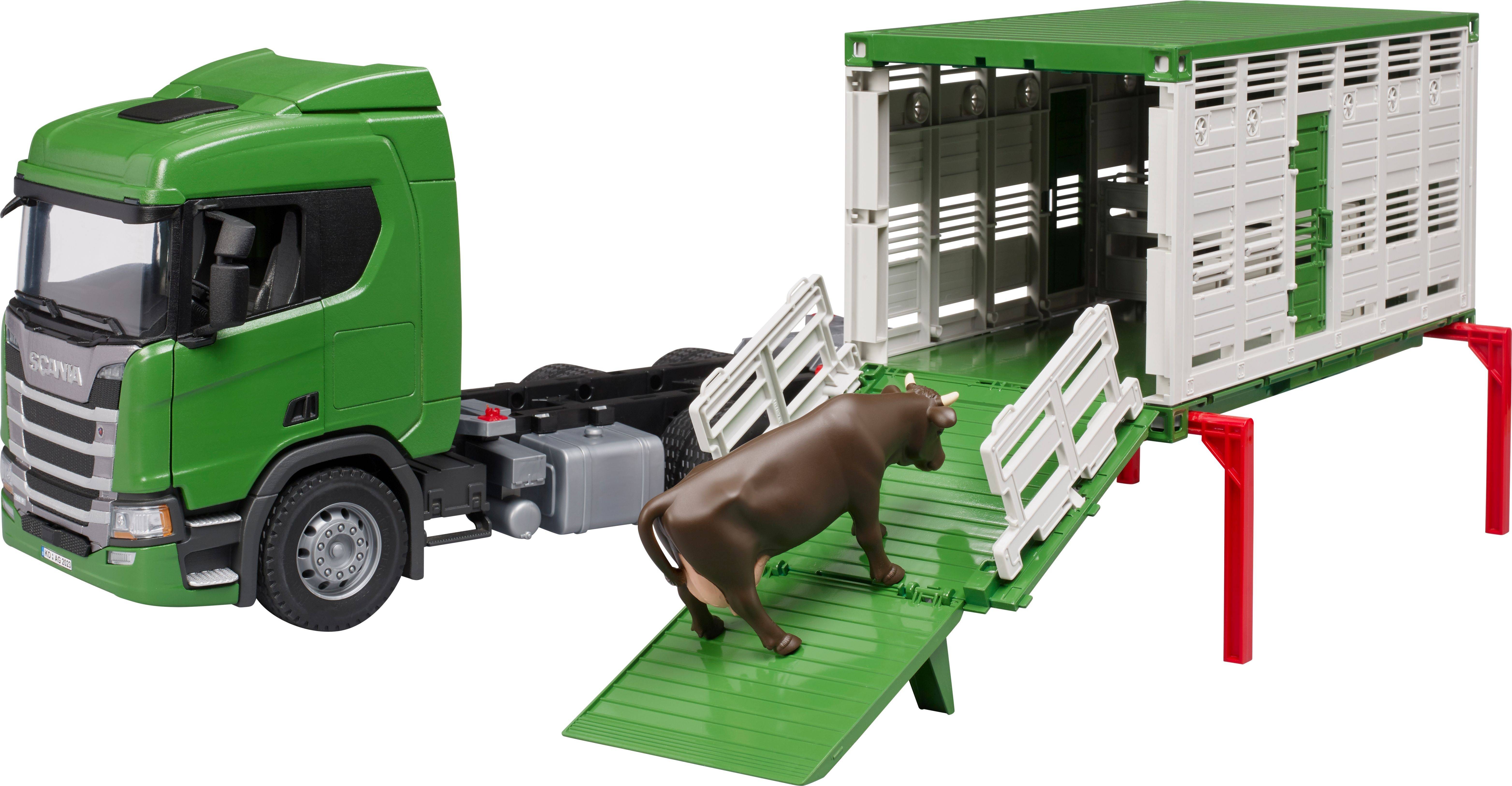 A green toy lorry with an animal trailer shows a cow walking up a ramp. The trailer is open for loading.