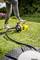A person is using a yellow water pump to irrigate the lawn in a garden. The surroundings are green and flowery.