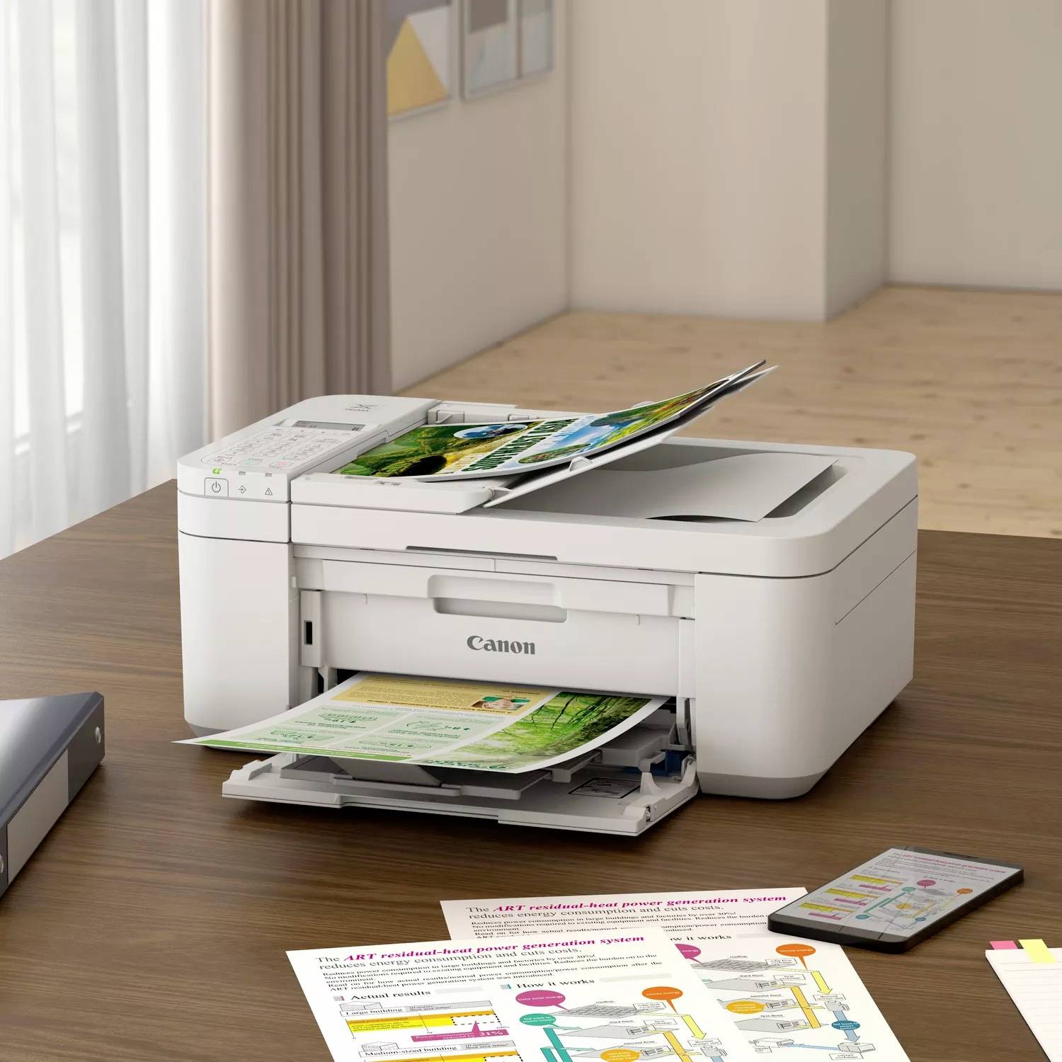 A printer sits on a table printing coloured pages. A smartphone is placed beside it. Blurred wall elements are visible in the background.