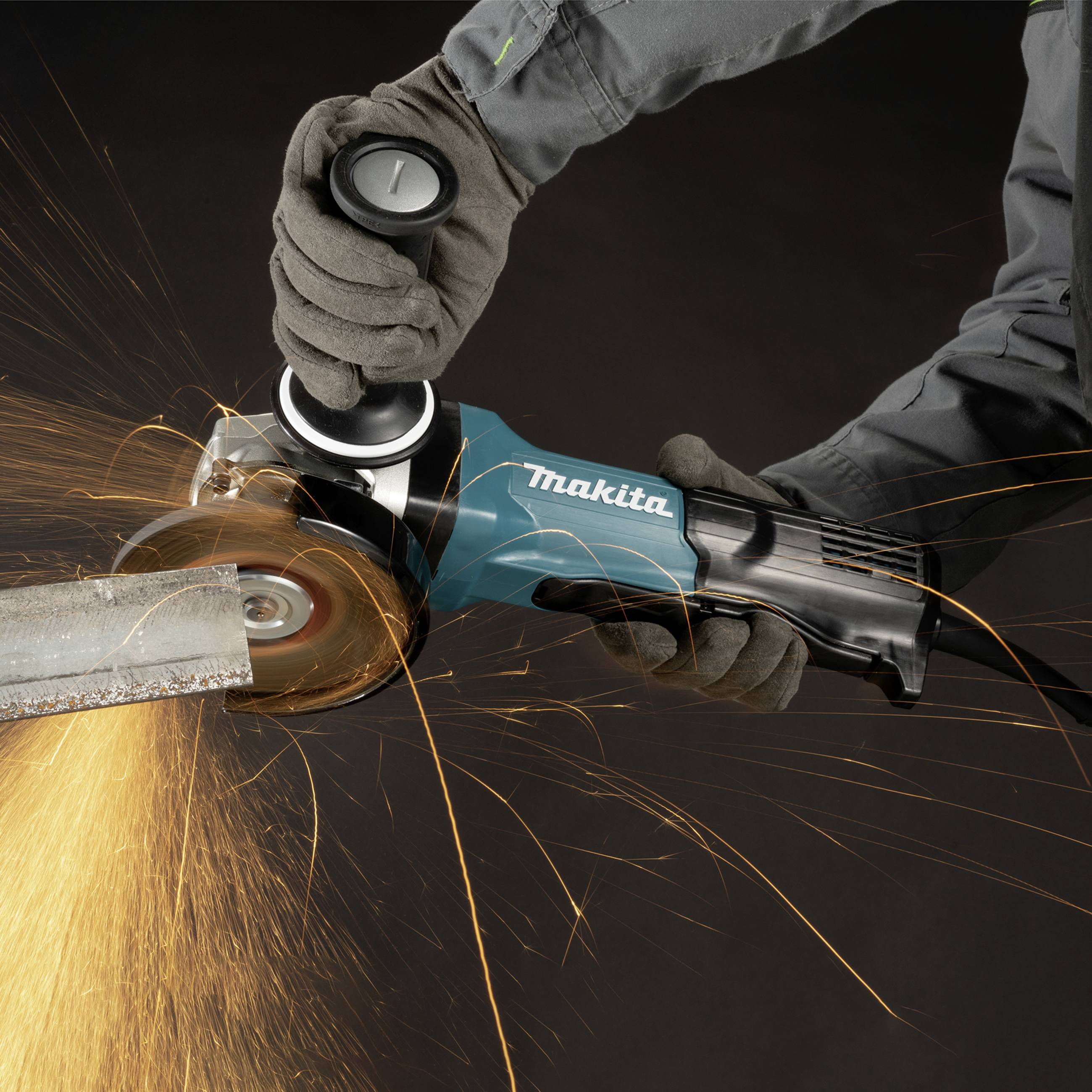 A skilled tradesman cuts a metal pipe with a blue angle grinder, sparks flying.